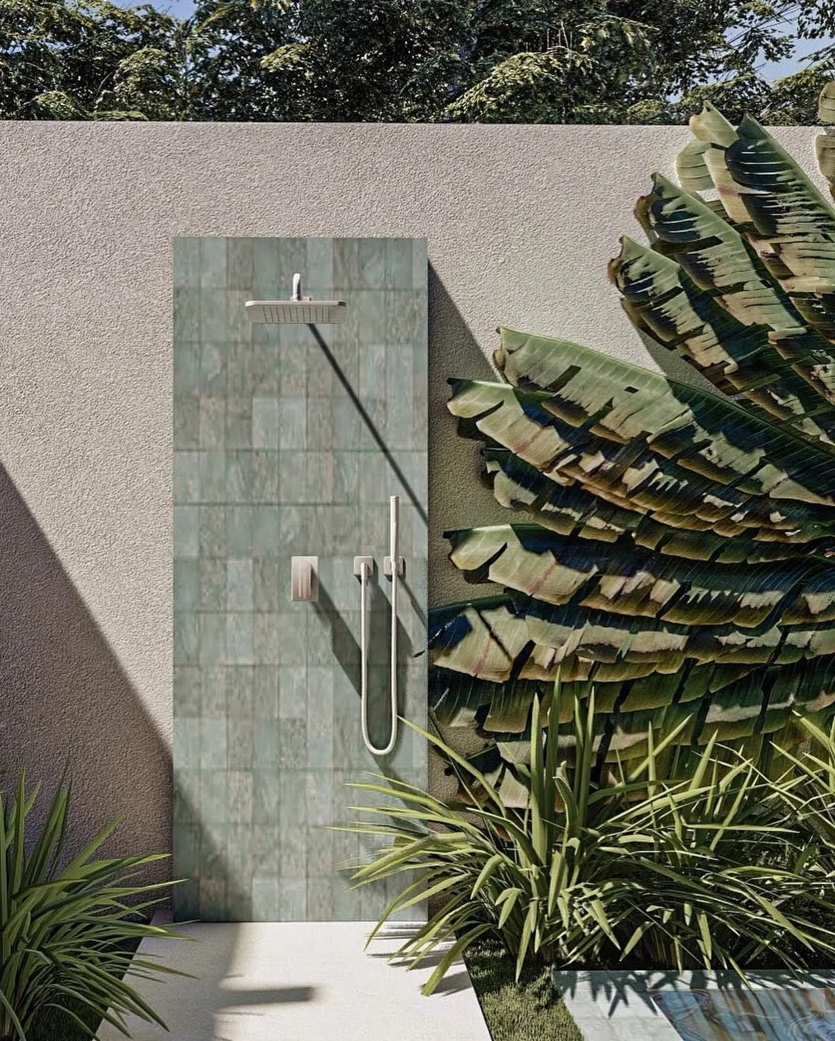 An outdoor shower with a green tiled wall, a rain shower head, and a handheld shower head, adjacent to large tropical plants and a concrete wall.