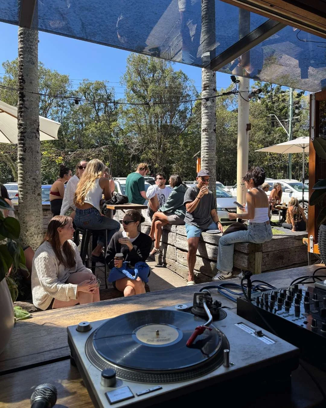 Group of people sitting in the sun at The Roadhouse with vinyl dj playing records