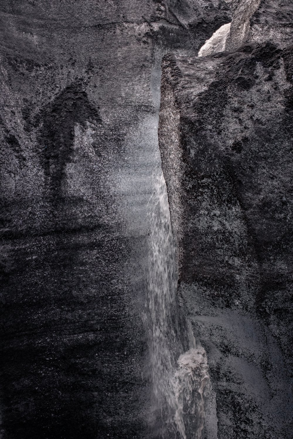A narrow canyon with dark, textured rock walls and water flowing through the center.