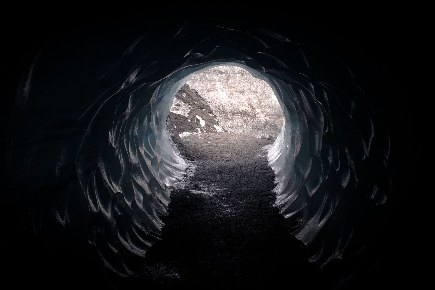 View from inside an ice tunnel looking outward to rocky terrain outside.