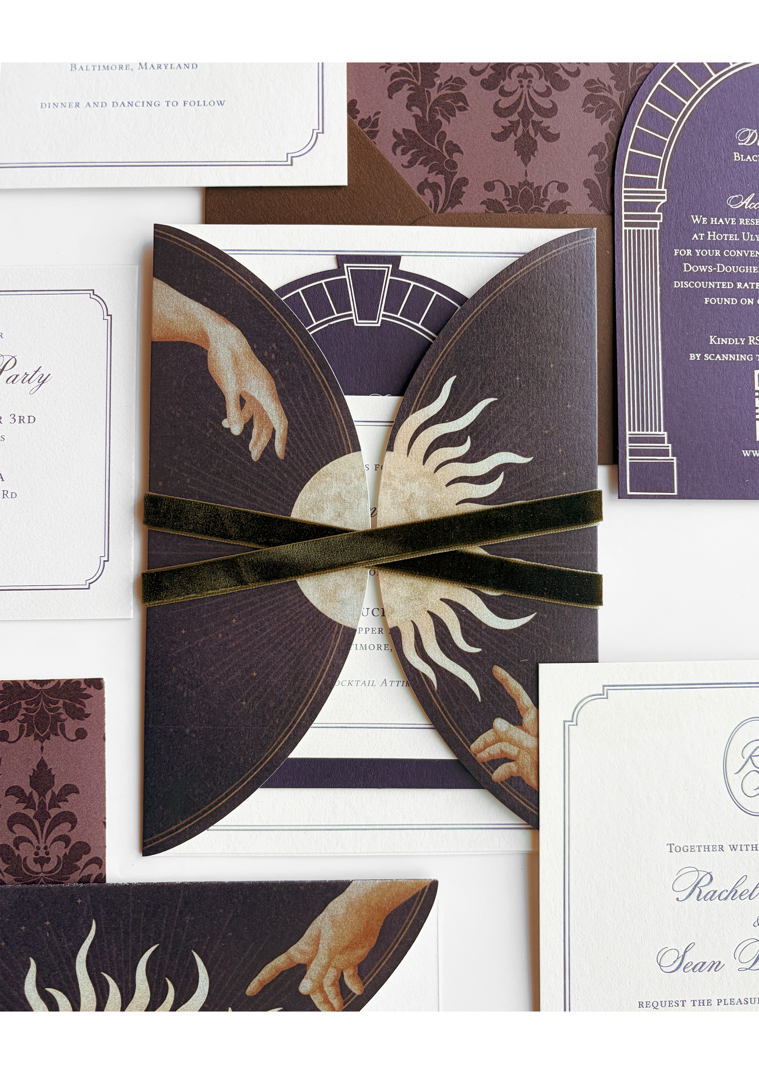 Celestial-inspired wedding invitation suite featuring deep plum and cream tones, Renaissance-style illustrated hands, sun motifs, velvet ribbon detailing, and layered arched stationery with romantic old-world design elements.
