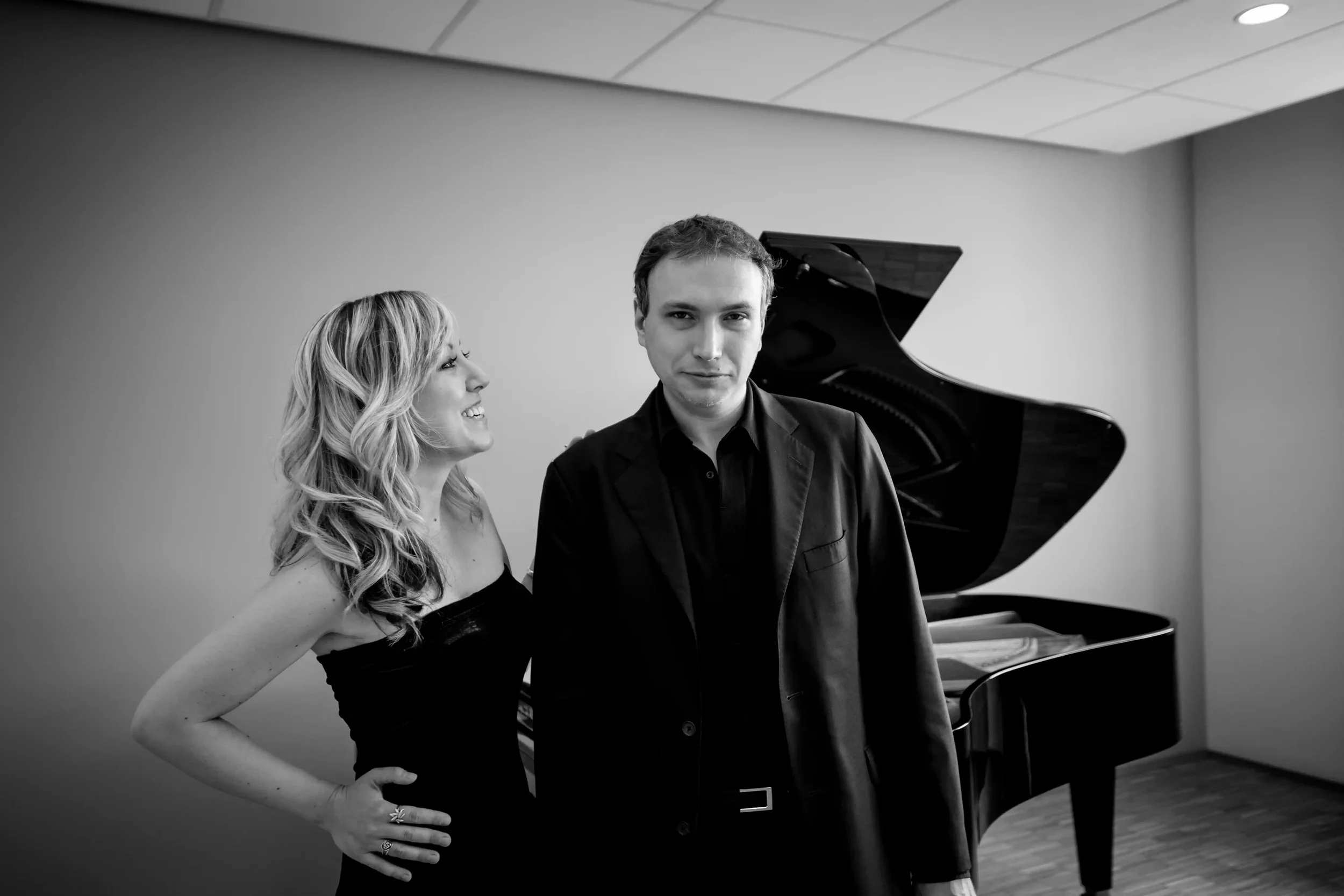young woman and young man posing in front of a piano smiling