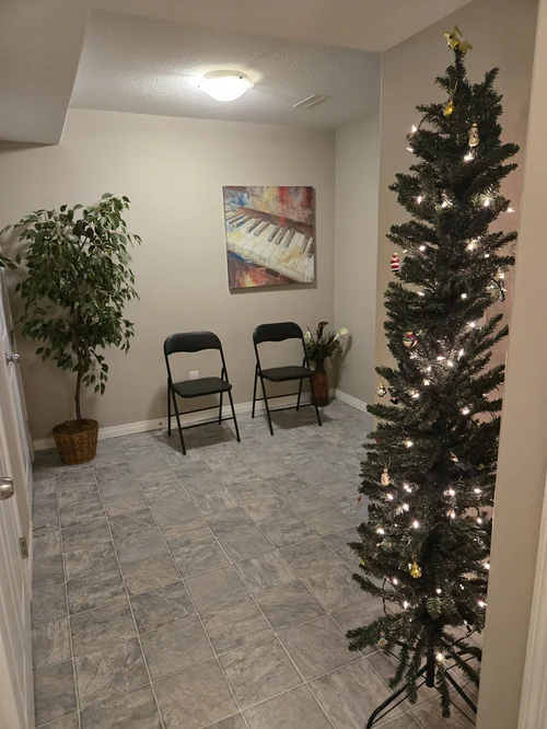 a room with two chairs and an artificial tree, showing a Christmas tree in the corner