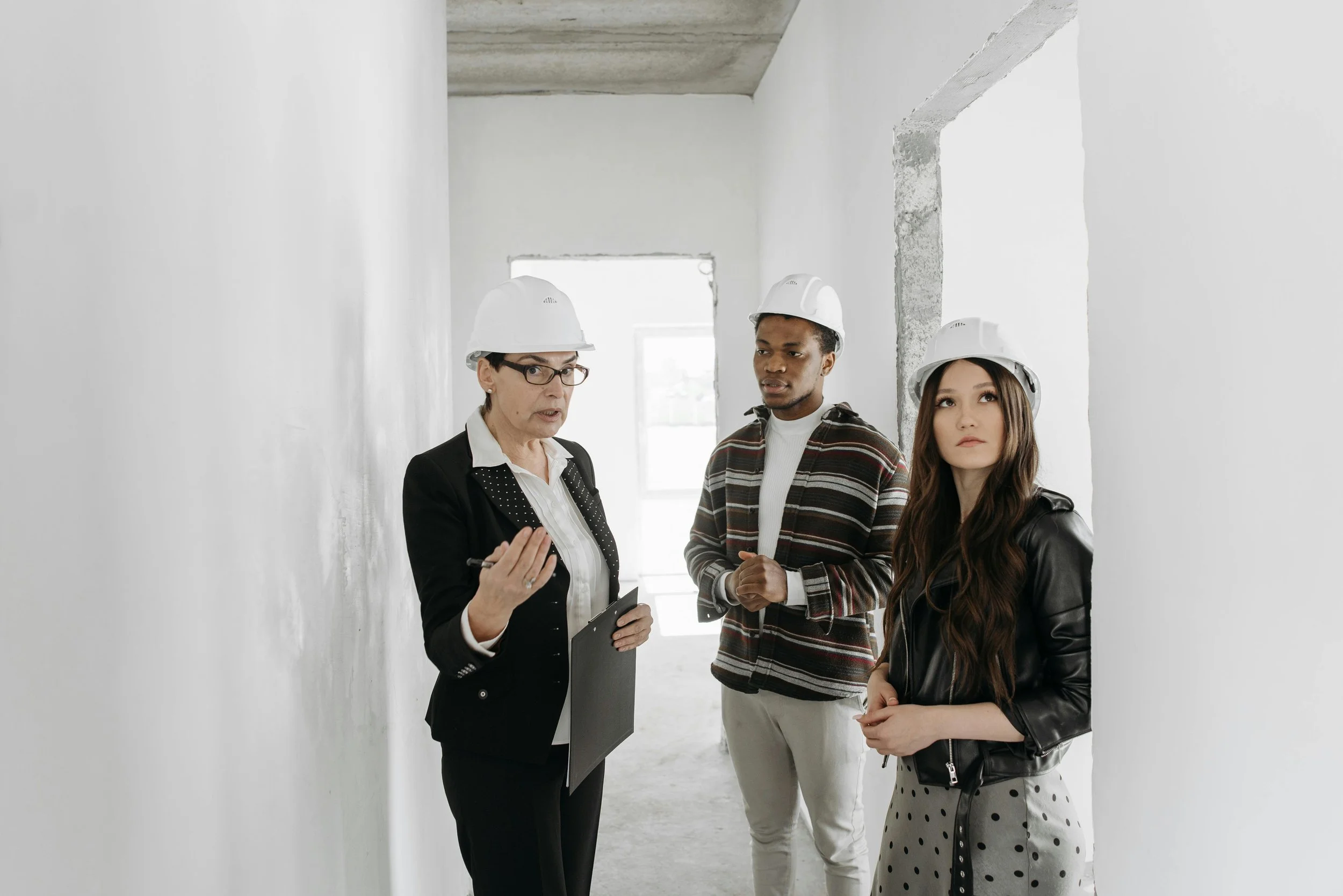 A team of people, one man and two women, walking through a home that is under construction. They are all wearing white hard hats.