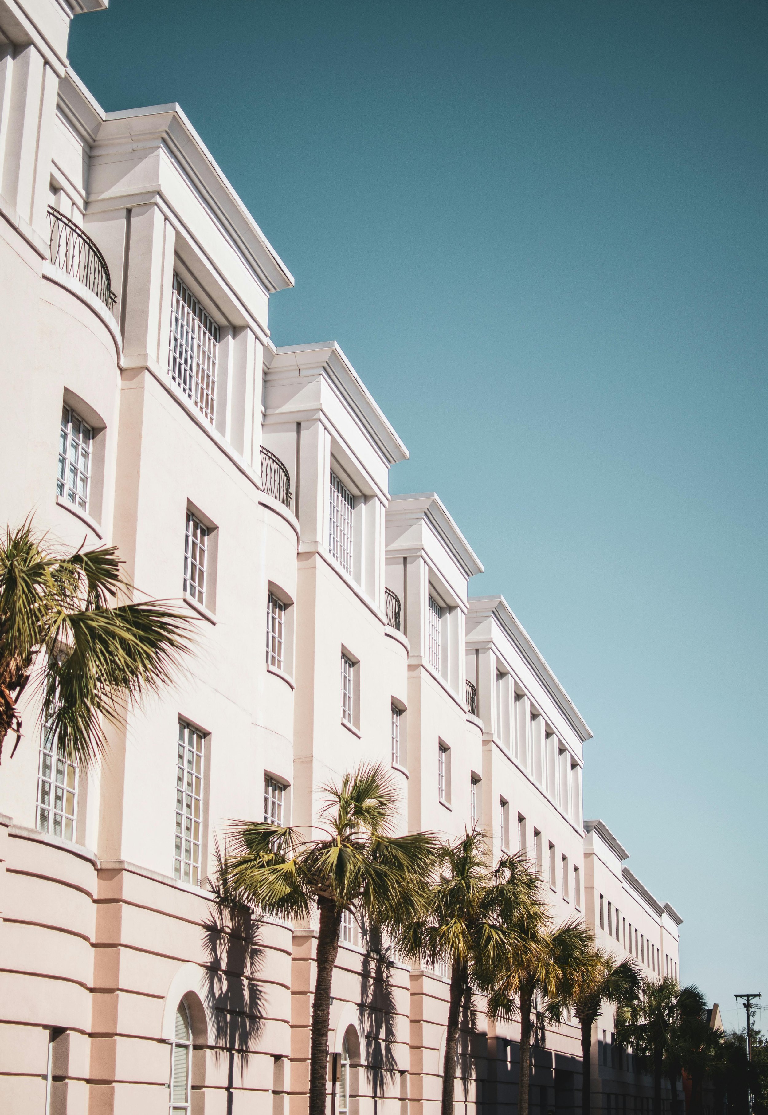 Sidewalk view of a white luxury condo complex based in a warm location with palm trees.