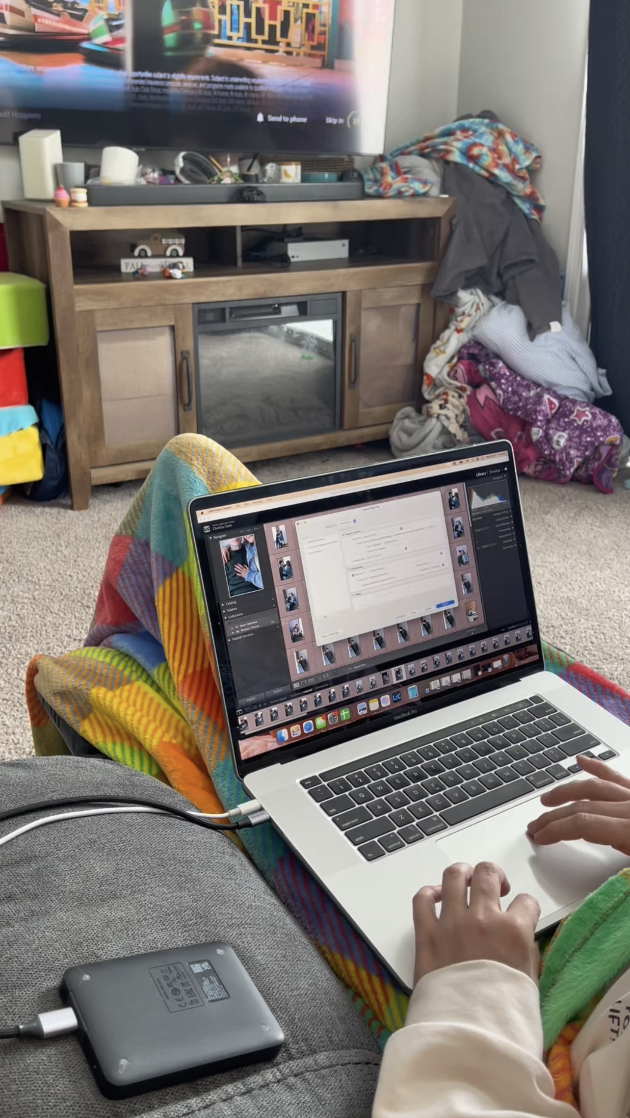 Professional Michigan photographer editing a photo gallery on a laptop at home, working from a couch with Lightroom open, showcasing behind-the-scenes photo editing workflow for family, wedding, and branding photography sessions.