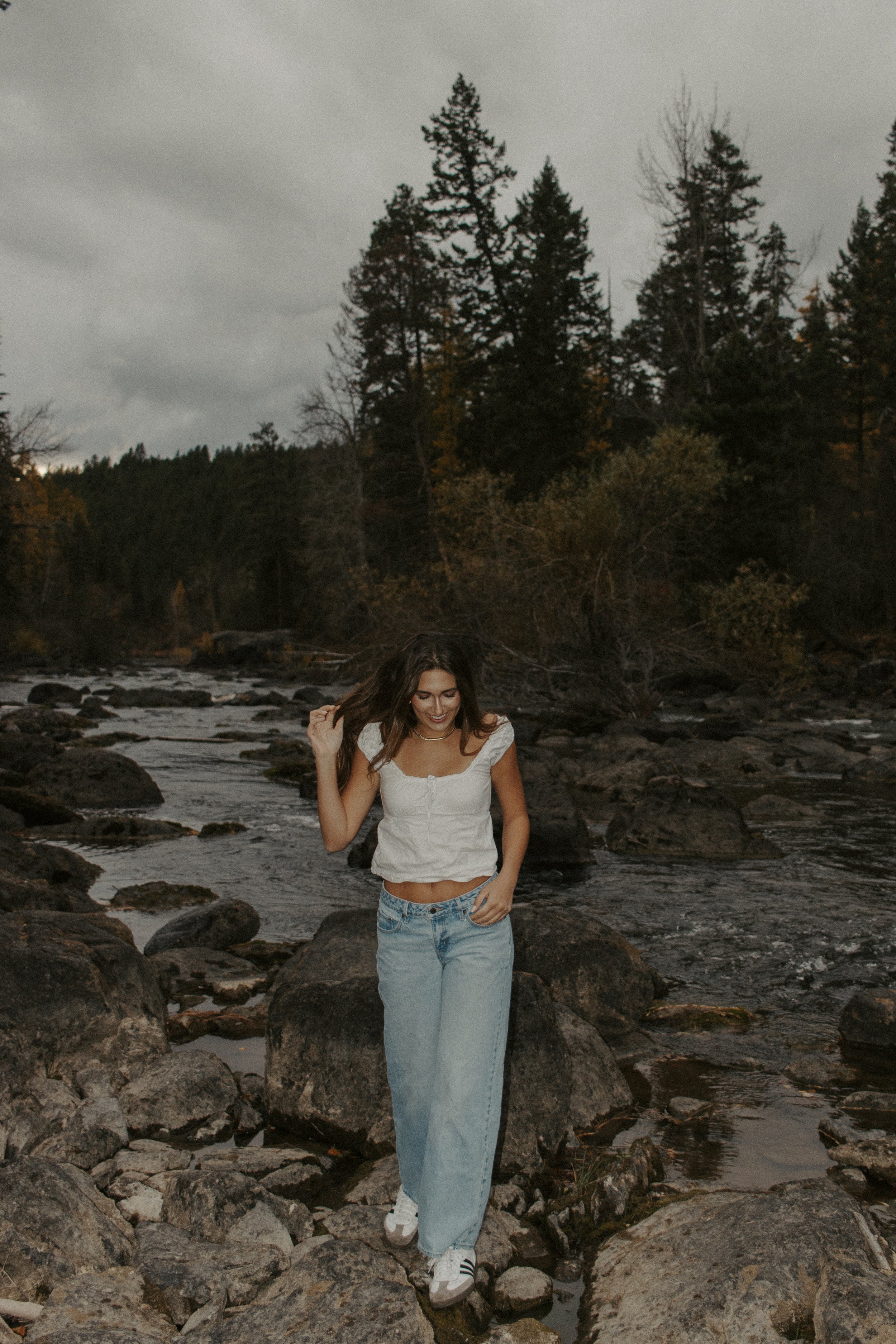 girl walks on rocks looking down with hand in hair