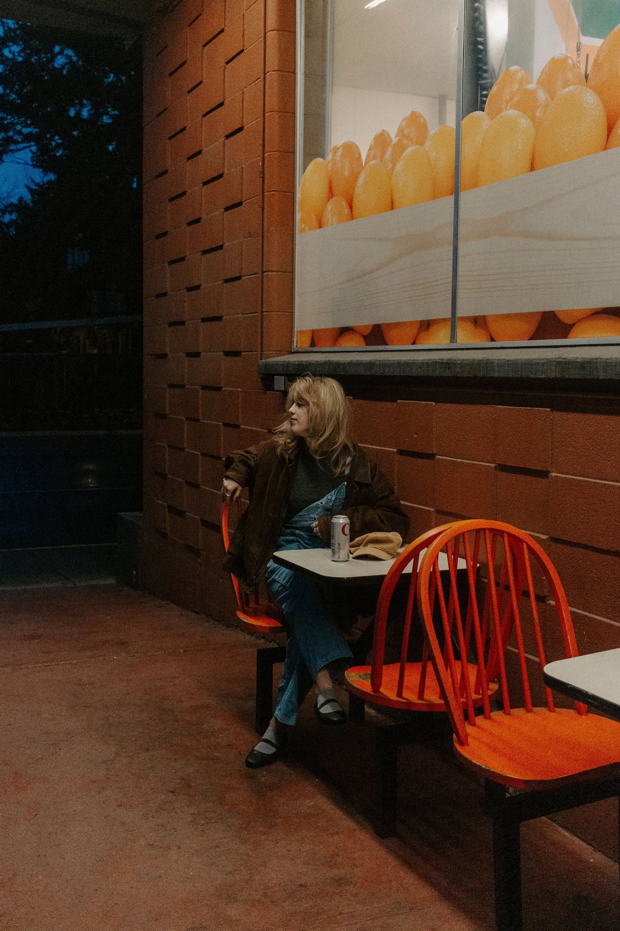 Girl sits in orange chair at table outside grocery store