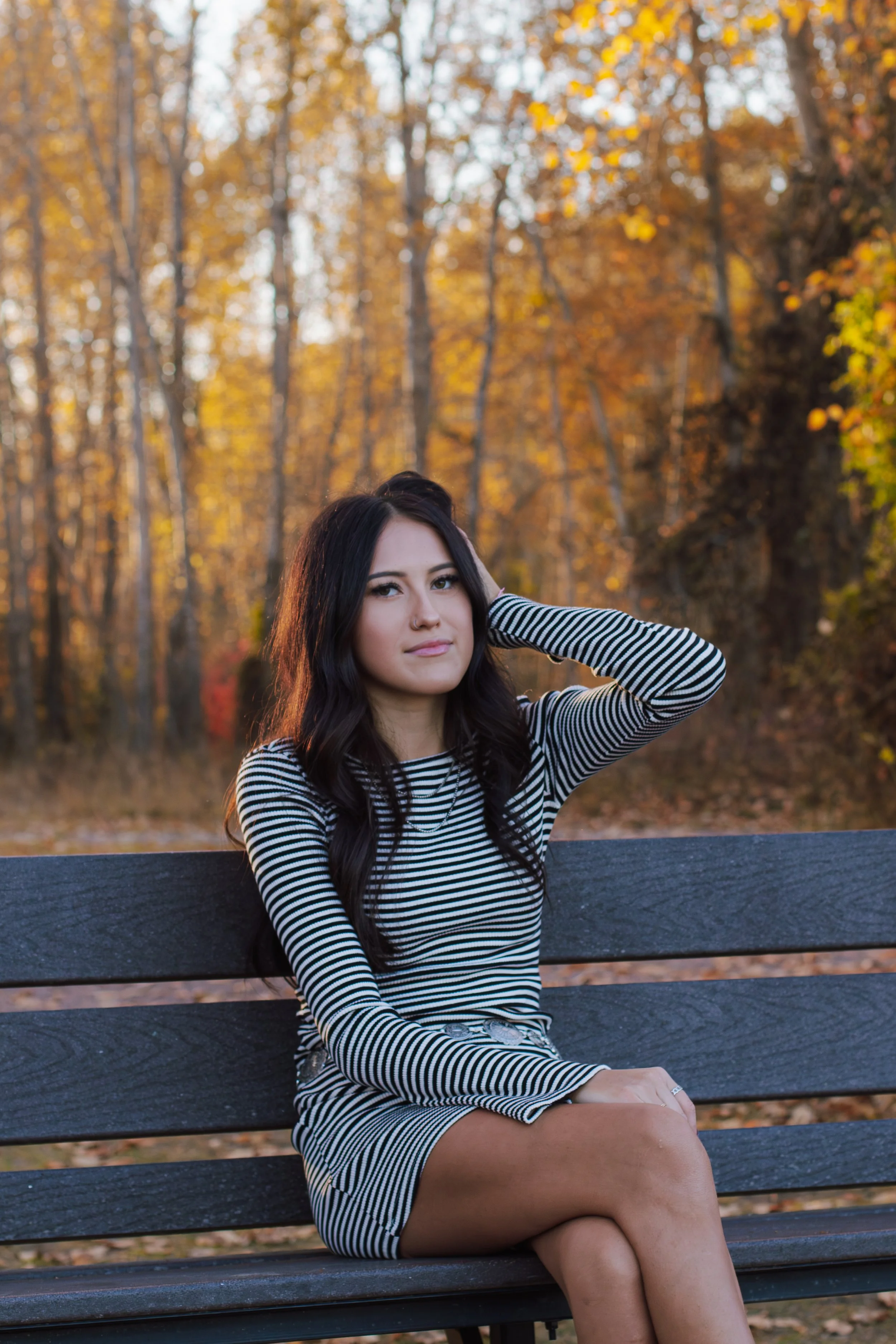 senior girl sits on black bench with hand in hair