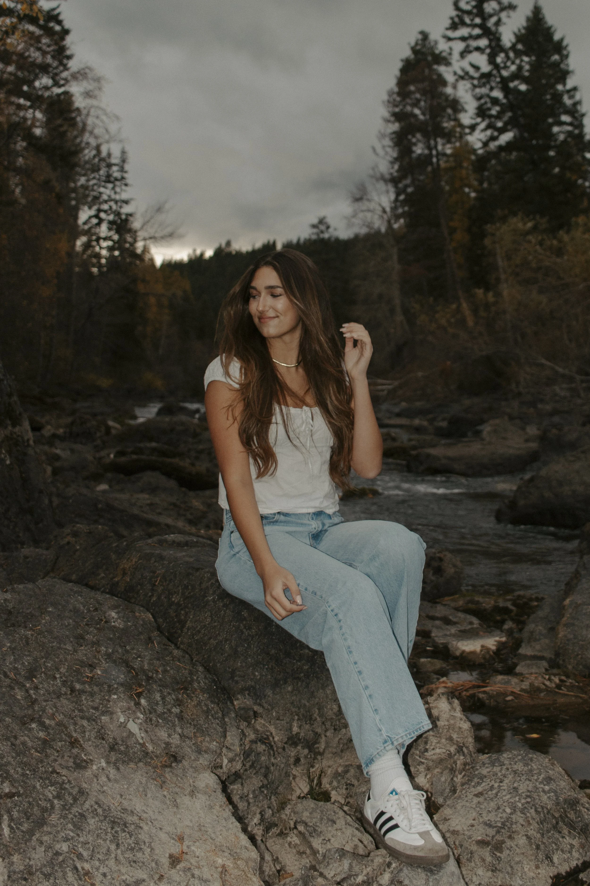 girl sits on rock by river looking to the side