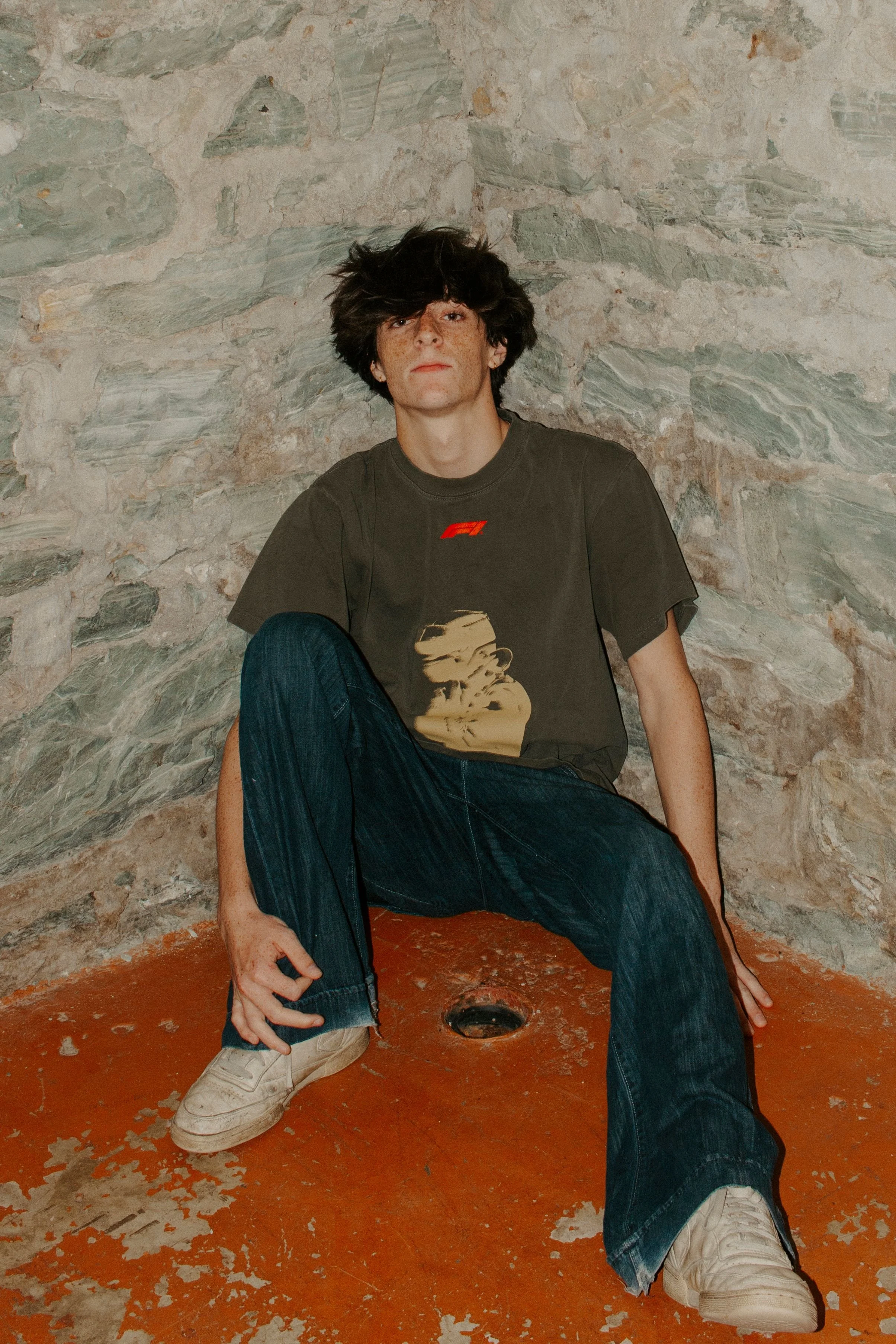 boy sits on floor against rock wall