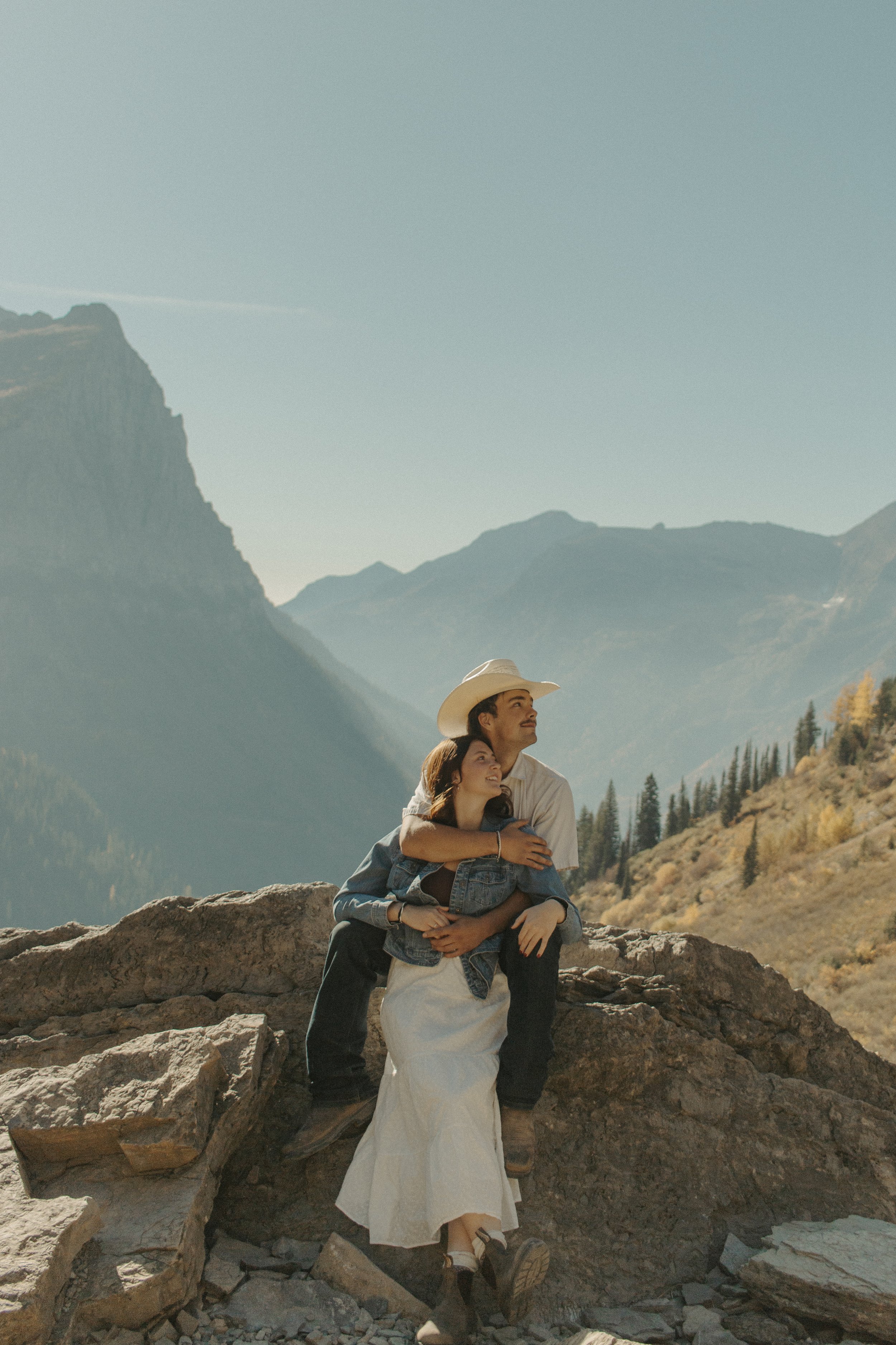 boy sits on rock while girl leans up against him looking at the sky