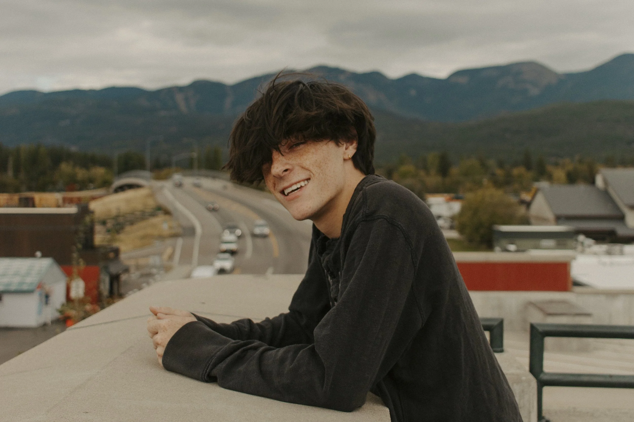 boy smiles leaning against cement in front of mountains