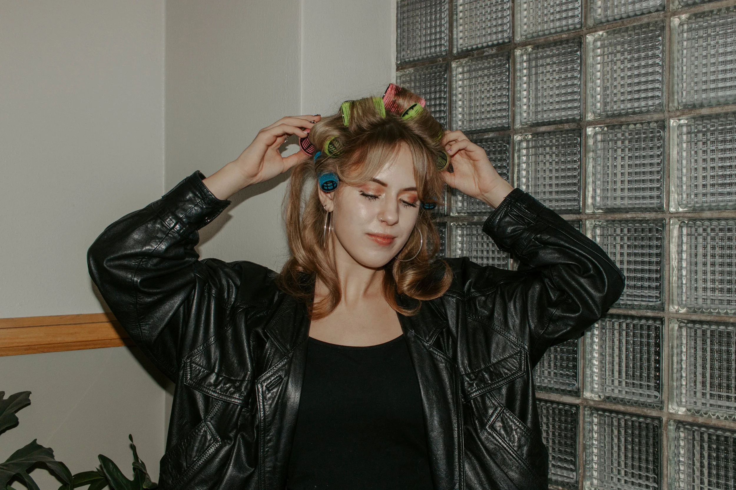 girl messes with curlers in her hair in front of glass backdrop