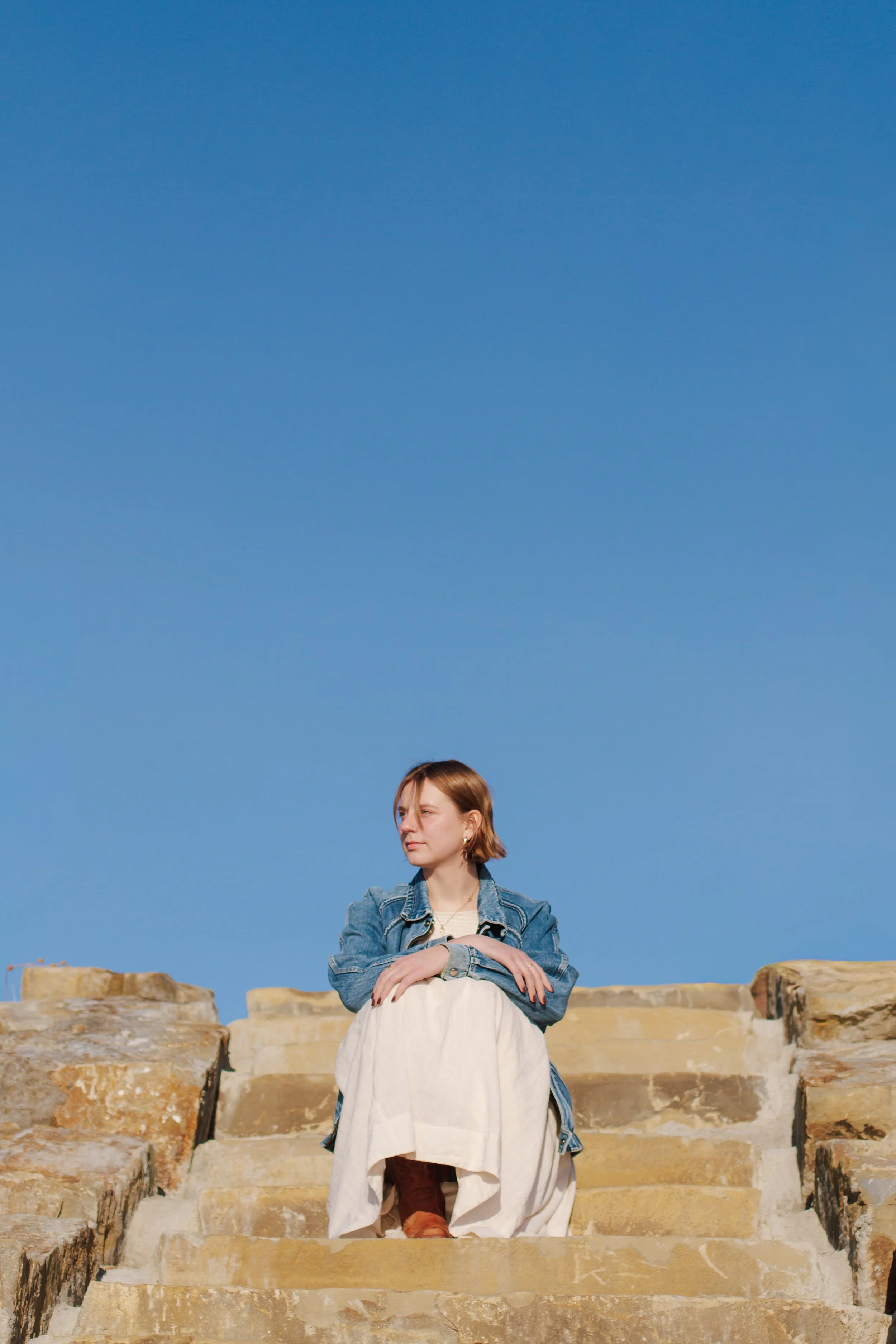 senior girl in dress looks to side while sitting on steps