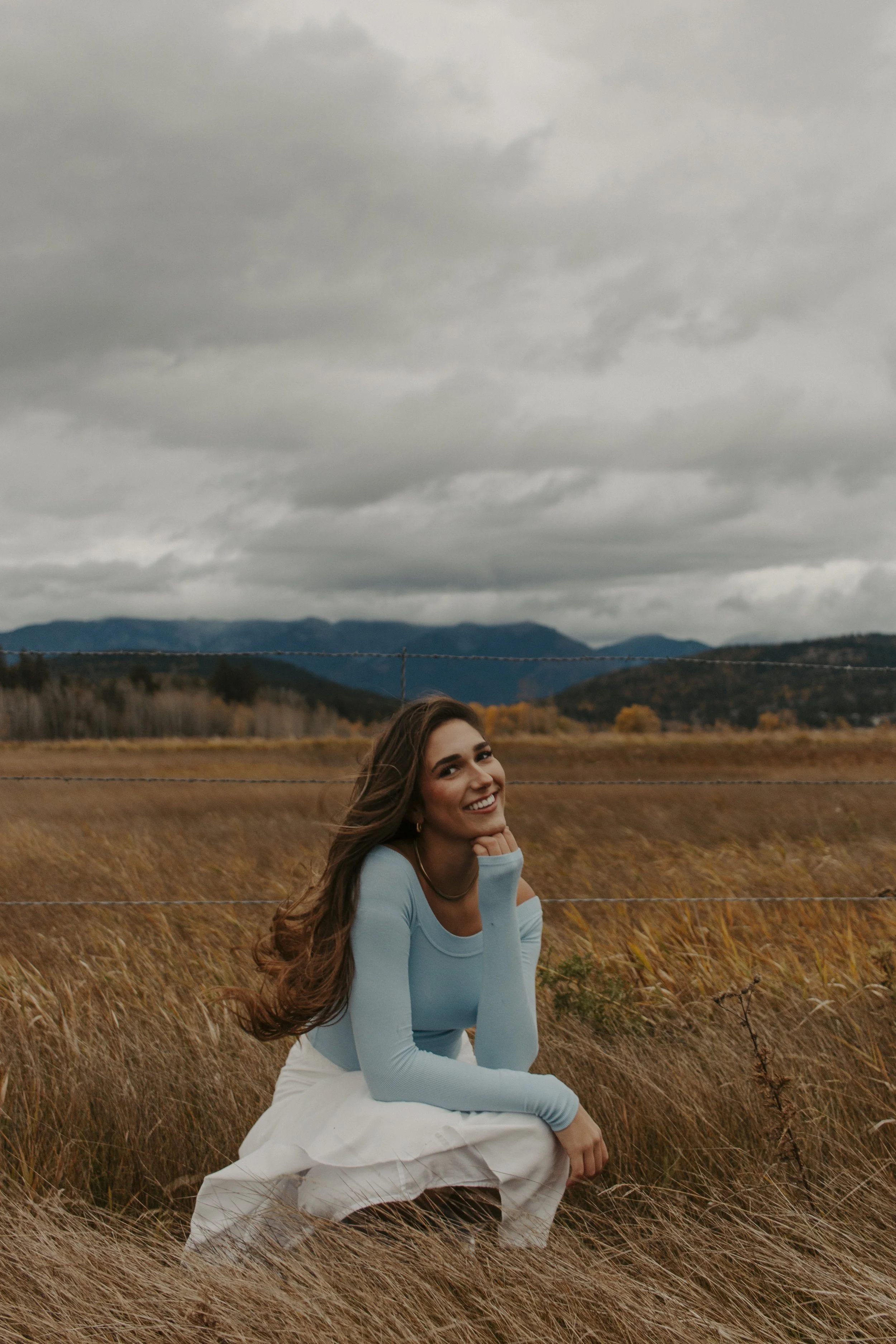 girl kneels in field resting head in hand