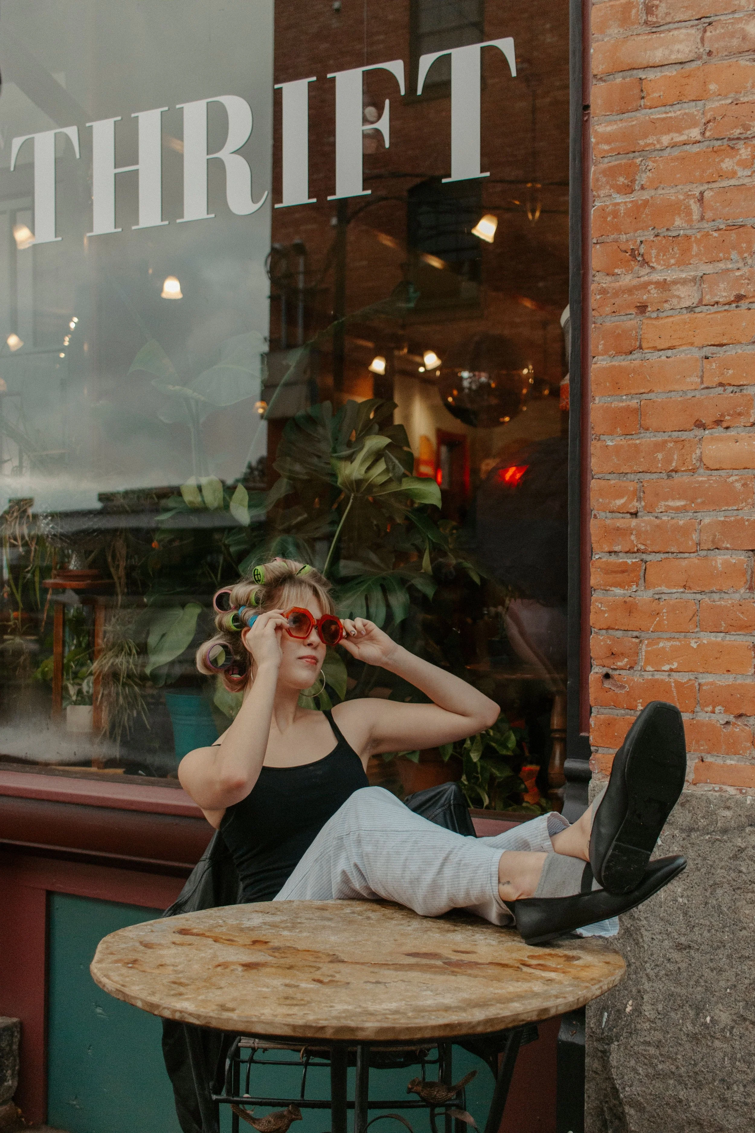 Girl sits with legs up on table putting on red glasses
