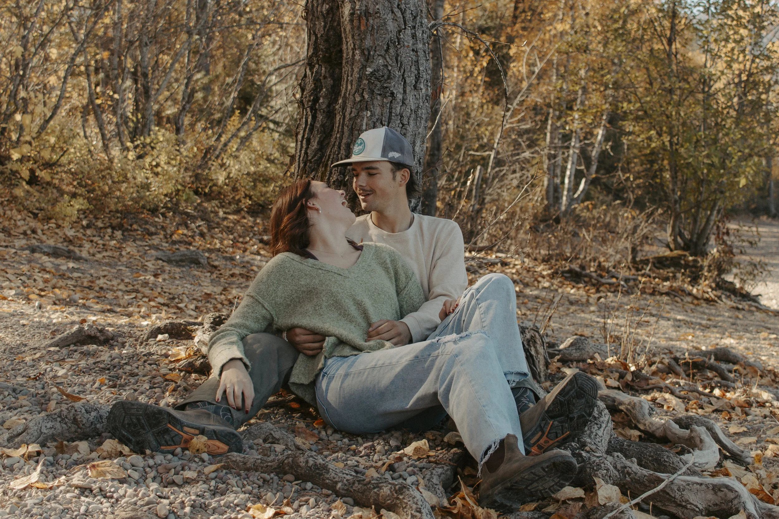 boy and girl sit against tree laughing at each other