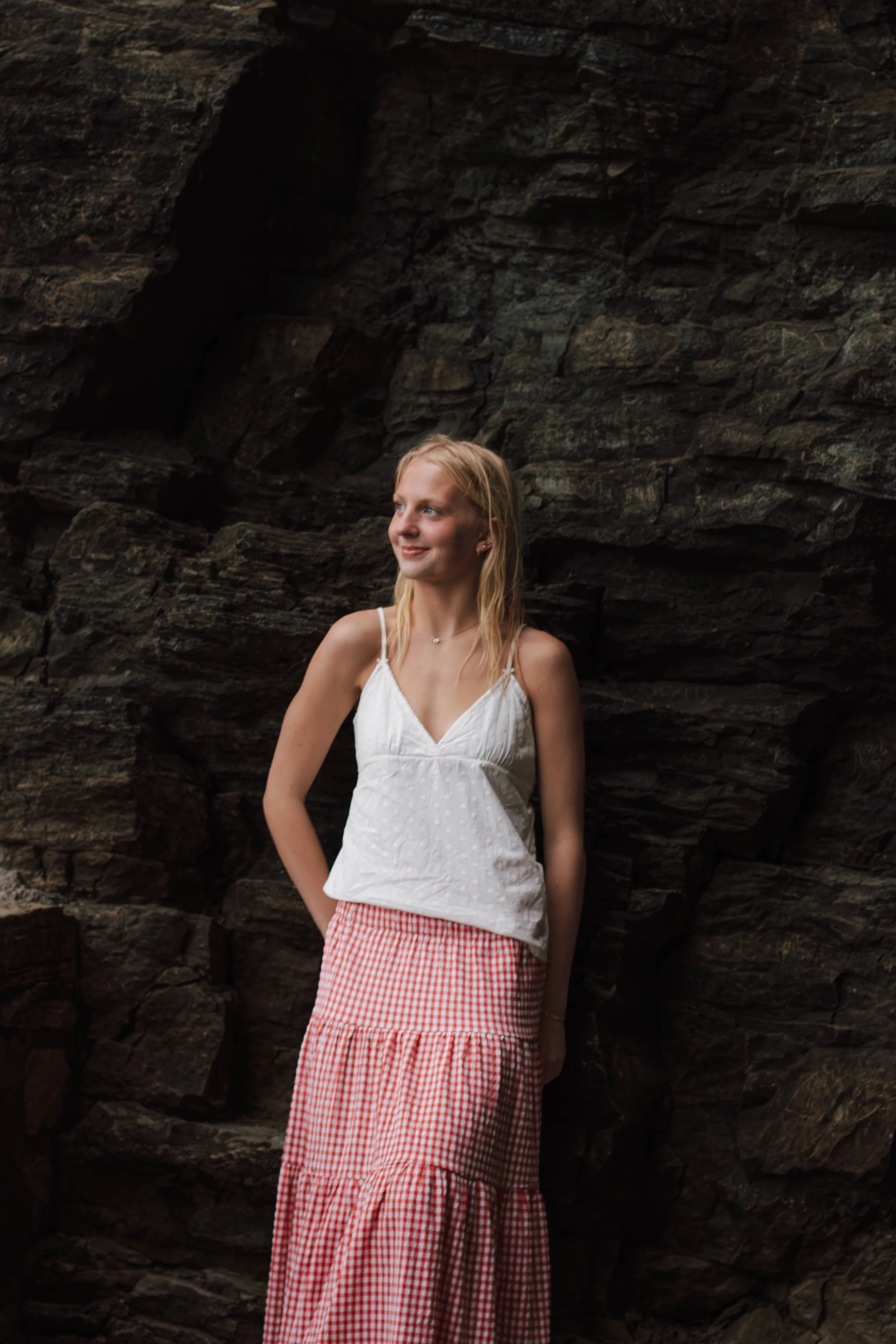 girl leans against rock and looks toward the sun