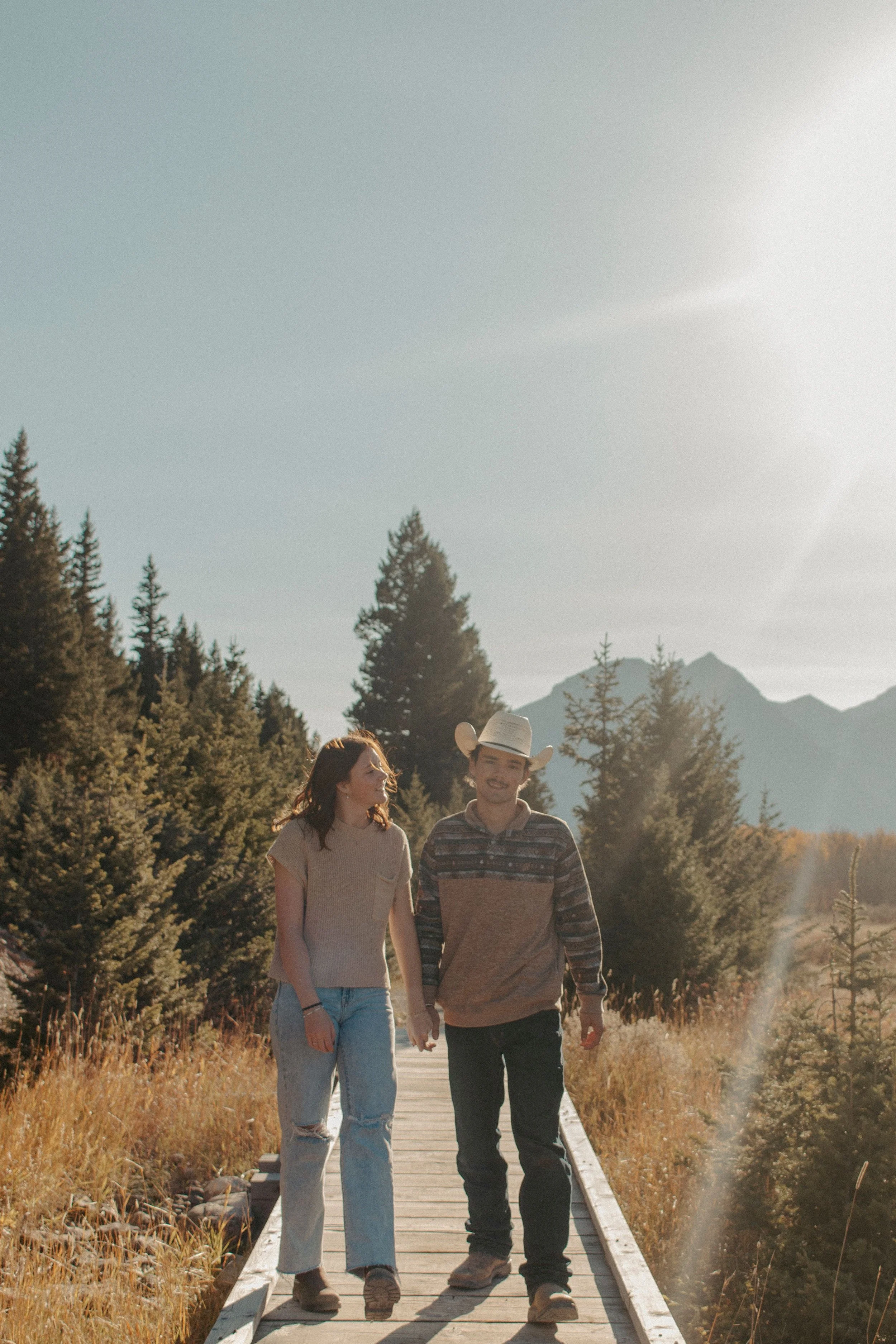 couple walks on boardwalk in field while smiling