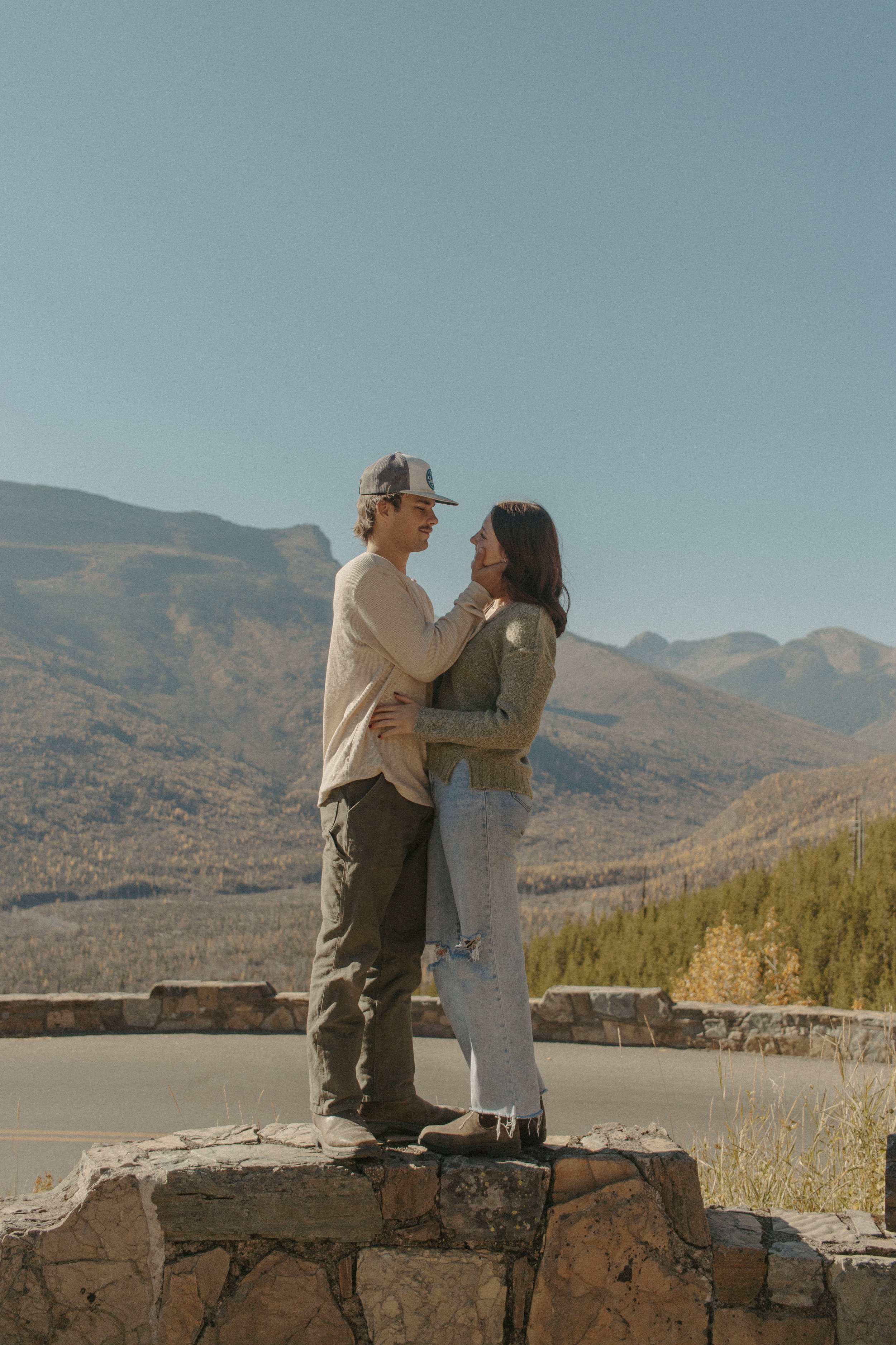 couple stands on rocks while the boy holds the girls face