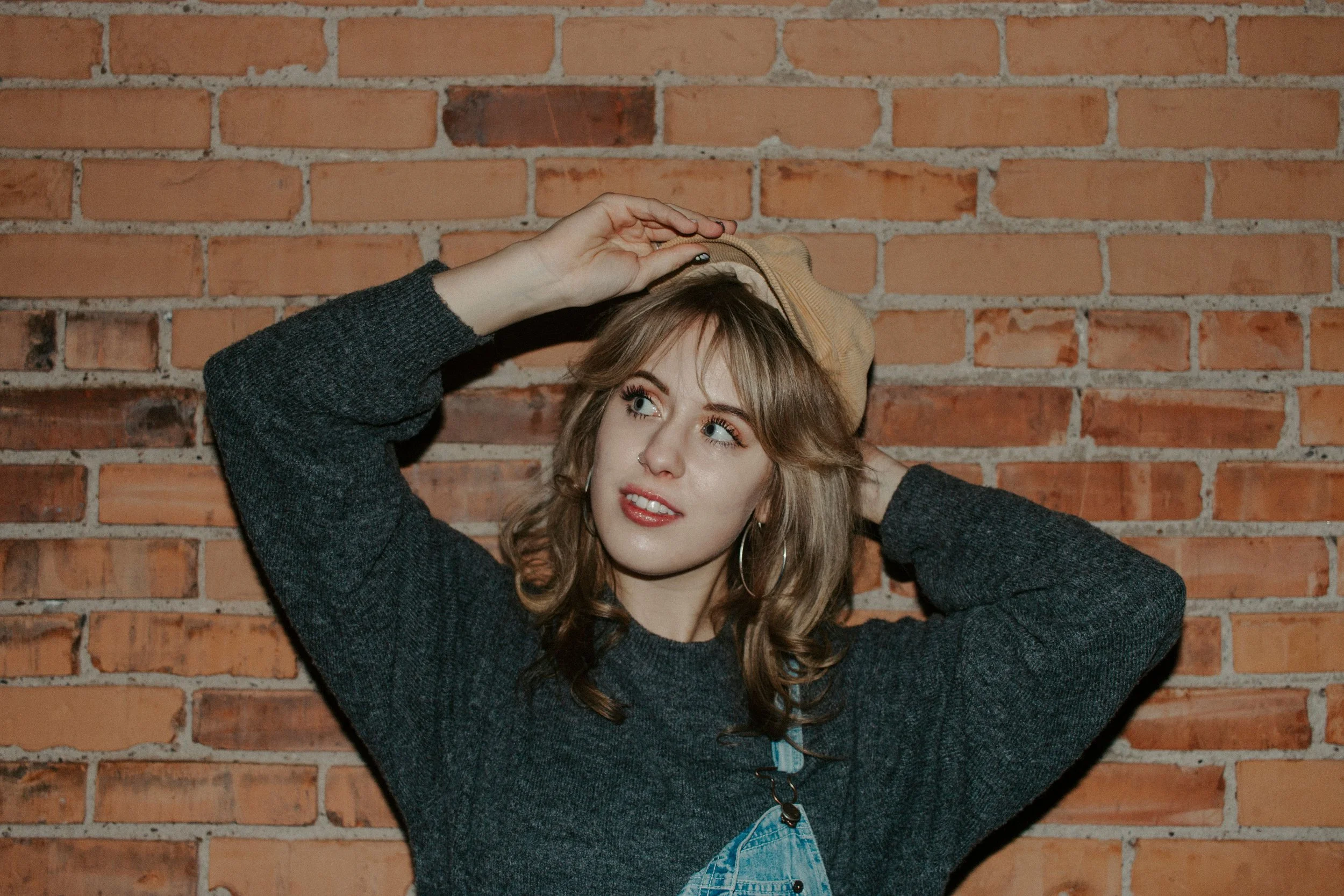 girl puts on hat in front of brick wall