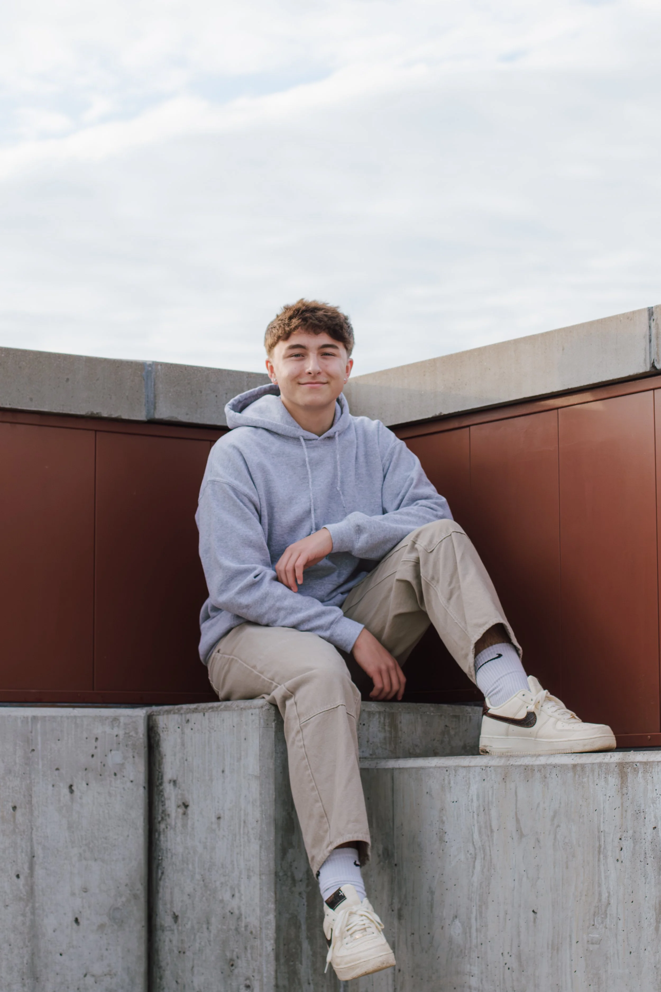 senior boy sits on concrete with one leg hanging