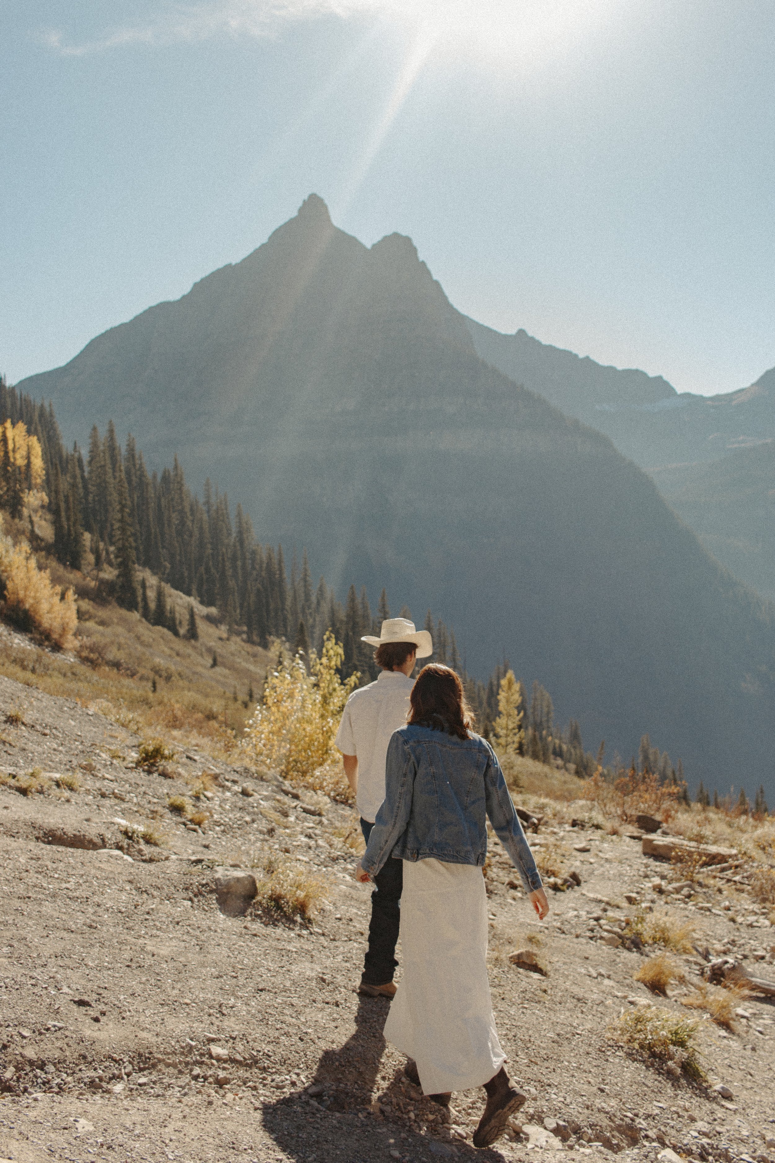 boy in cowboy hat and girl in white skirt walk down gravel trail