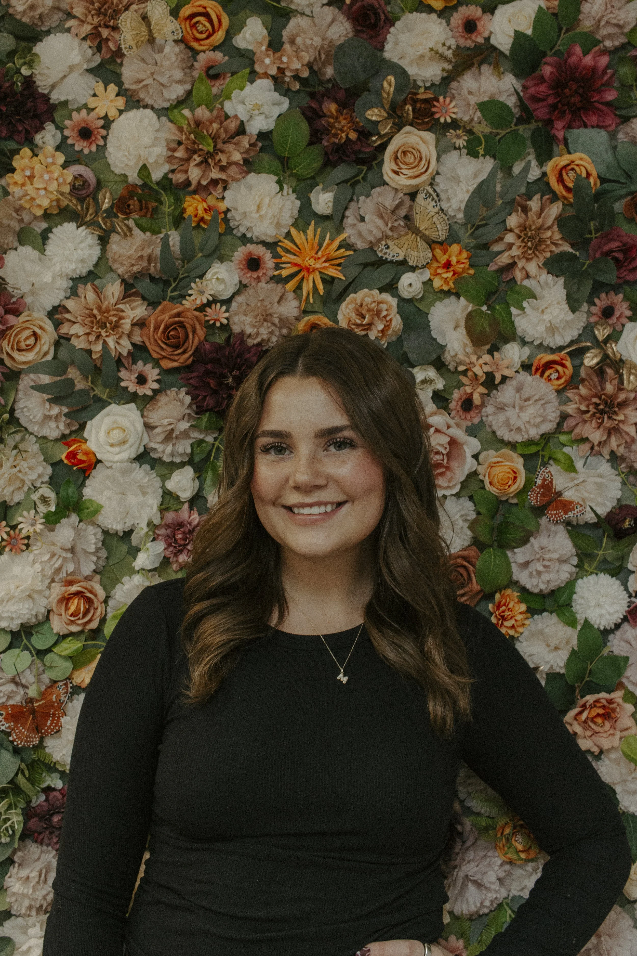 girl in black shirt smiles against flower wall