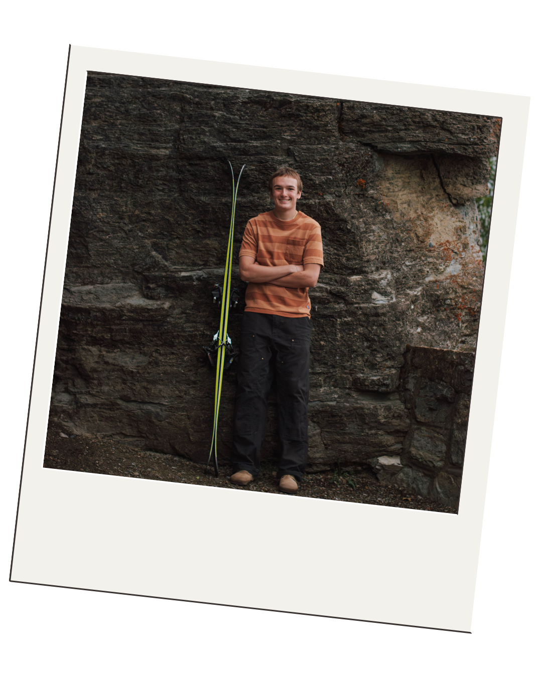 boy leans up against rocks with snow skiis