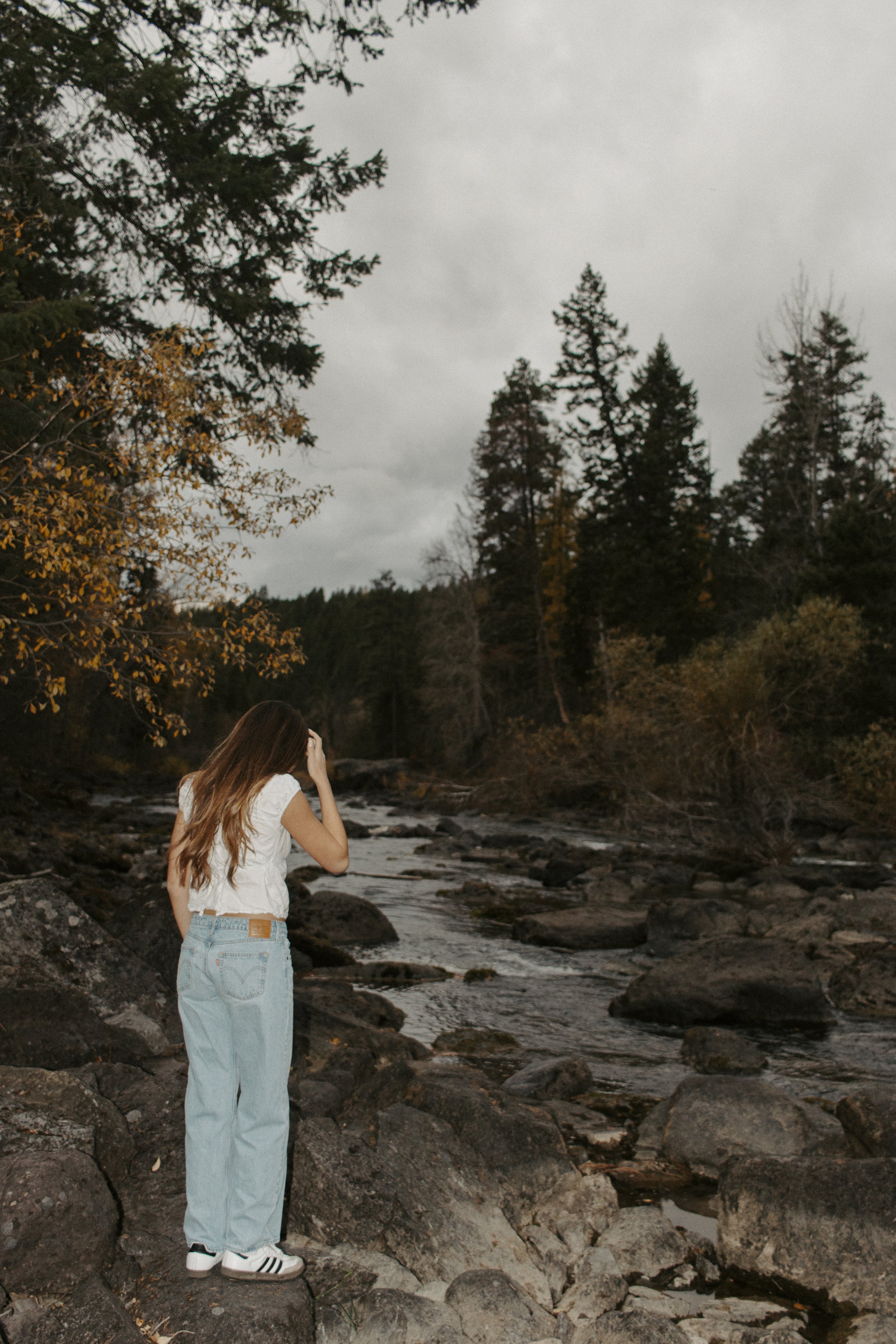 Girl in white shirt and jeans walks on rocks toward river