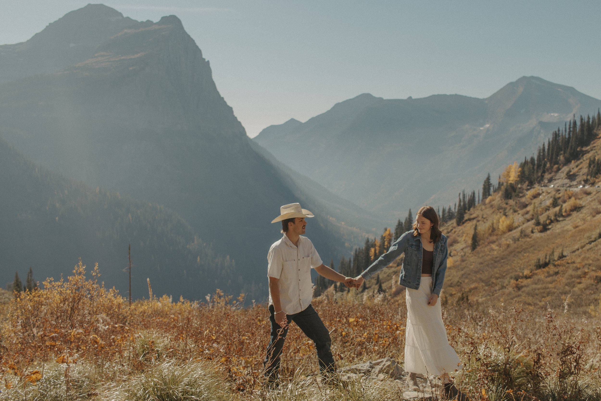 couple walks on path while holding hand in front of mountains
