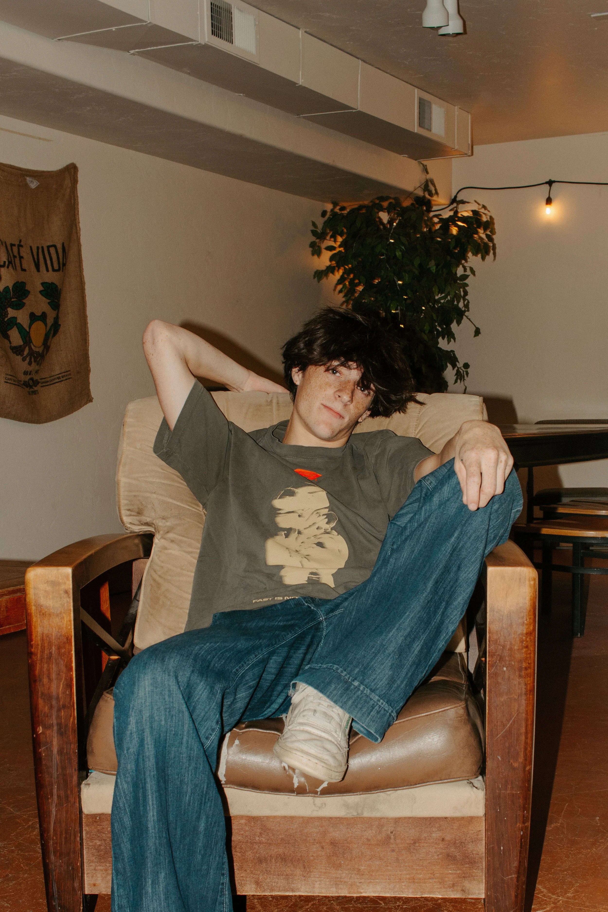 boy sits in coffee shop chair with his hand behind his head