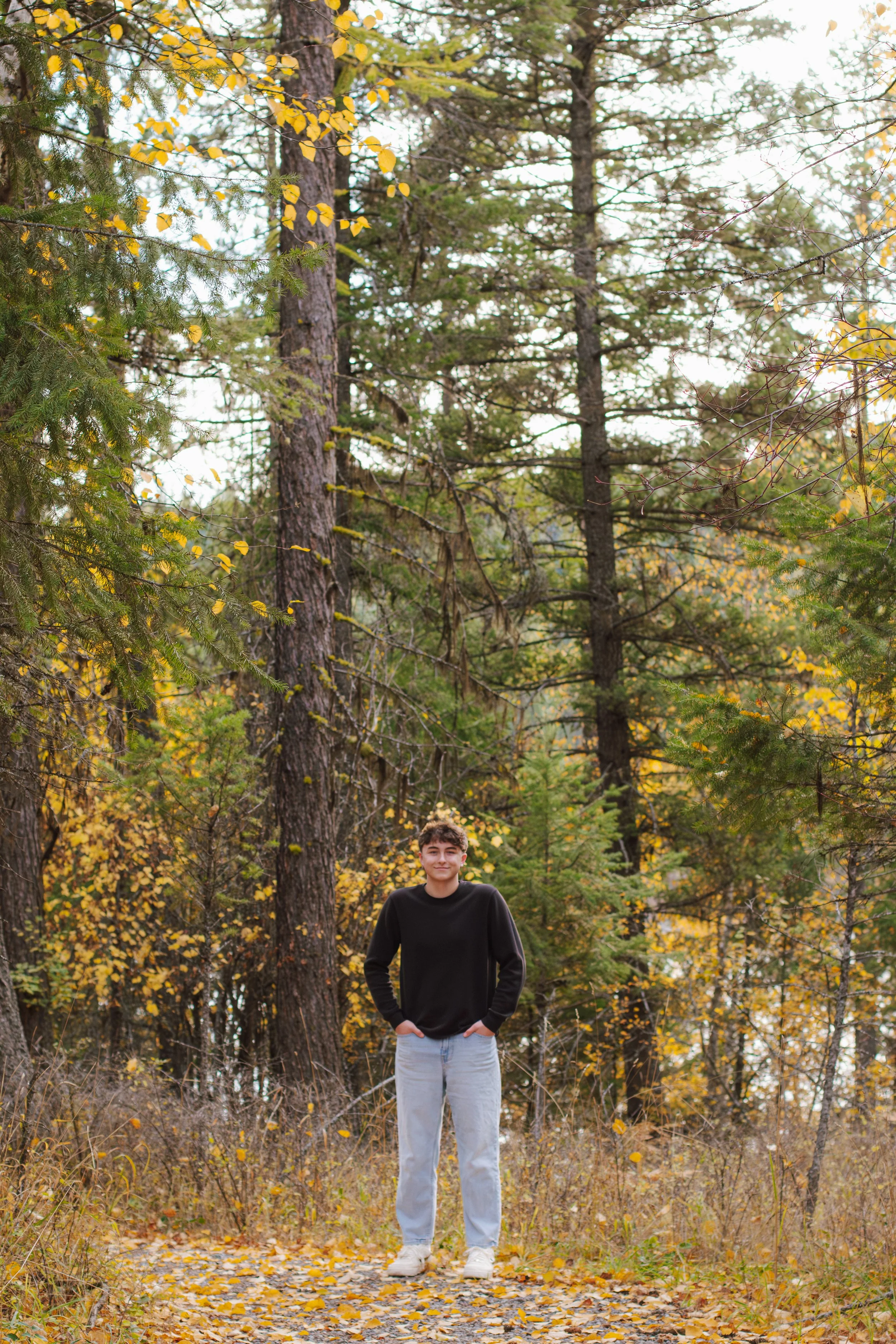 senior stands in center of trees in the fall