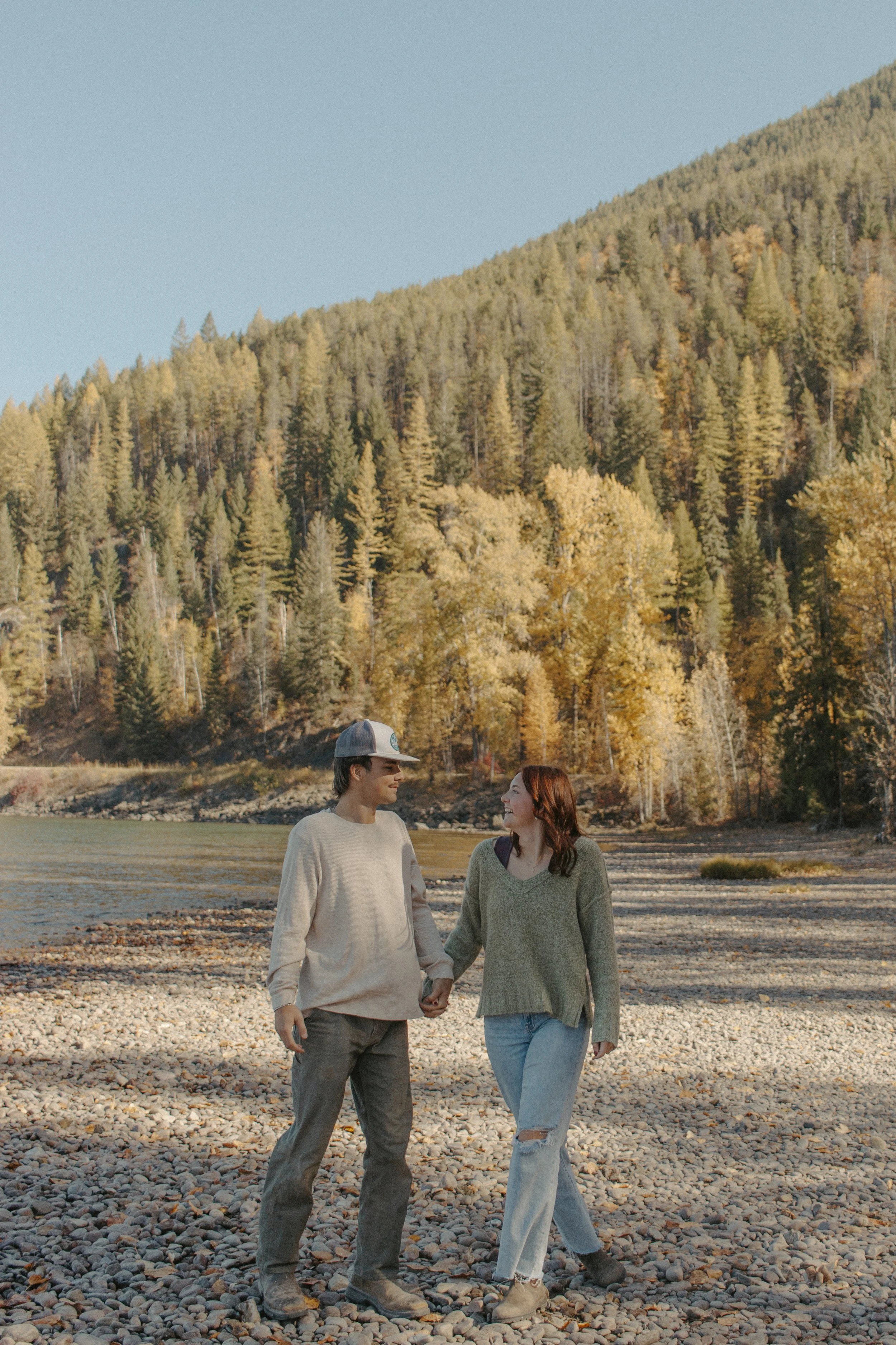 couples holds hands and walks on shoreline of lake