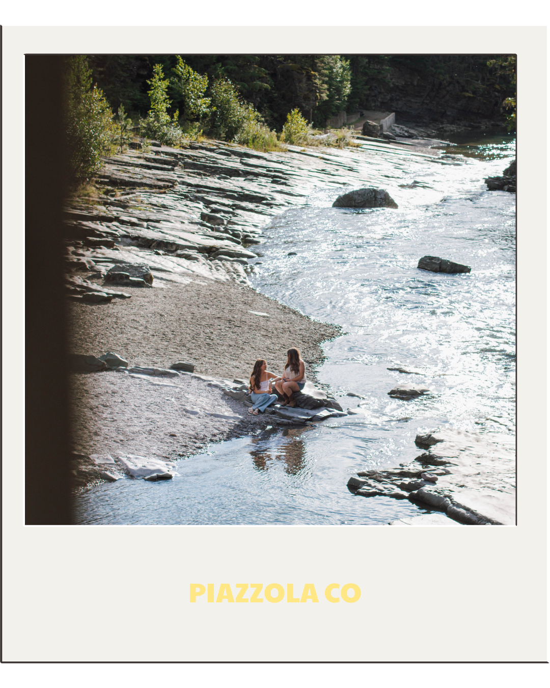two girls sit on a rock by the river