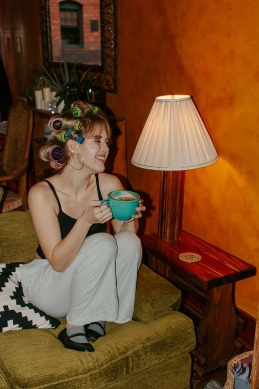 girl sits on green couch with legs up holding coffee