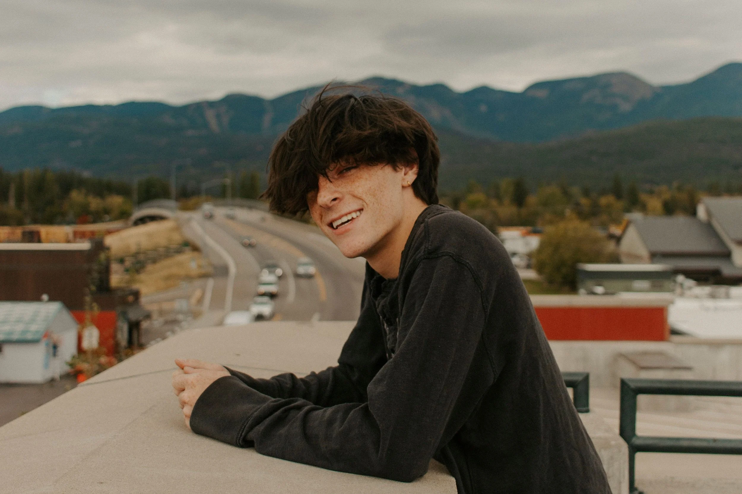 boy leans up against wall with mountains in the background