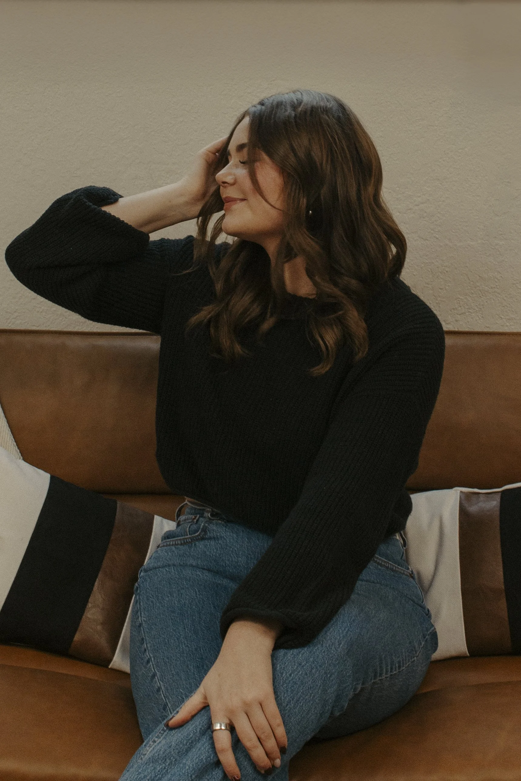 girll fixes her hair and smiles to the side while sitting on brown couch