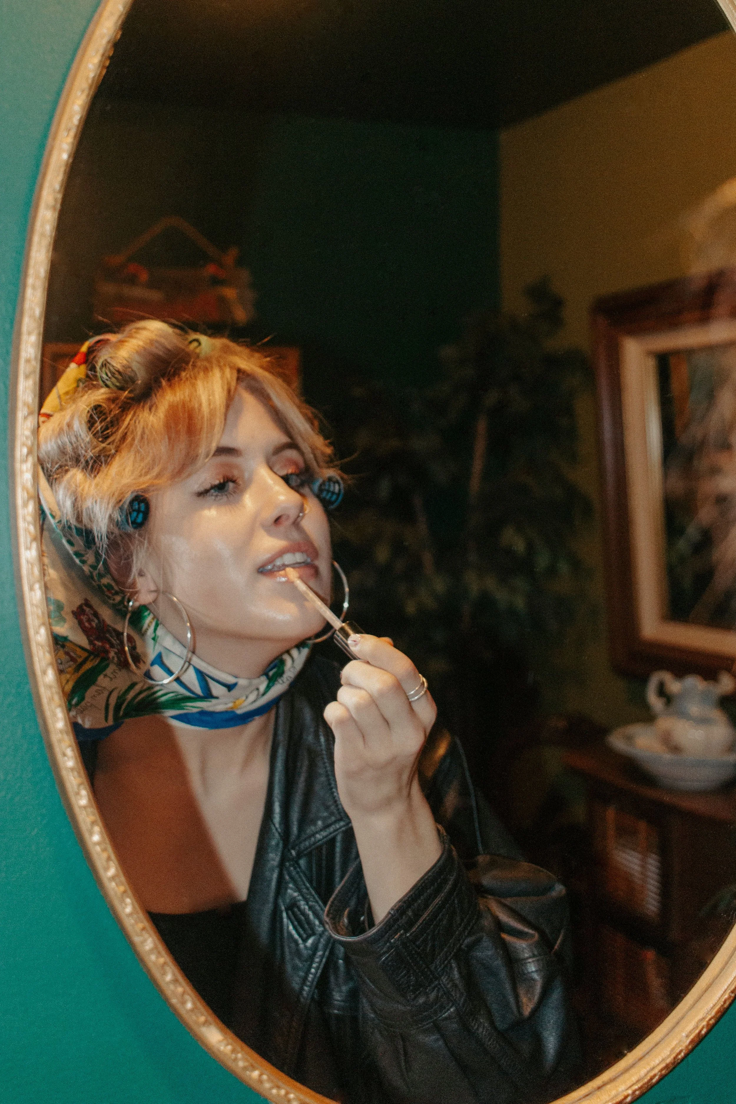 Girl puts on lip gloss in mirror