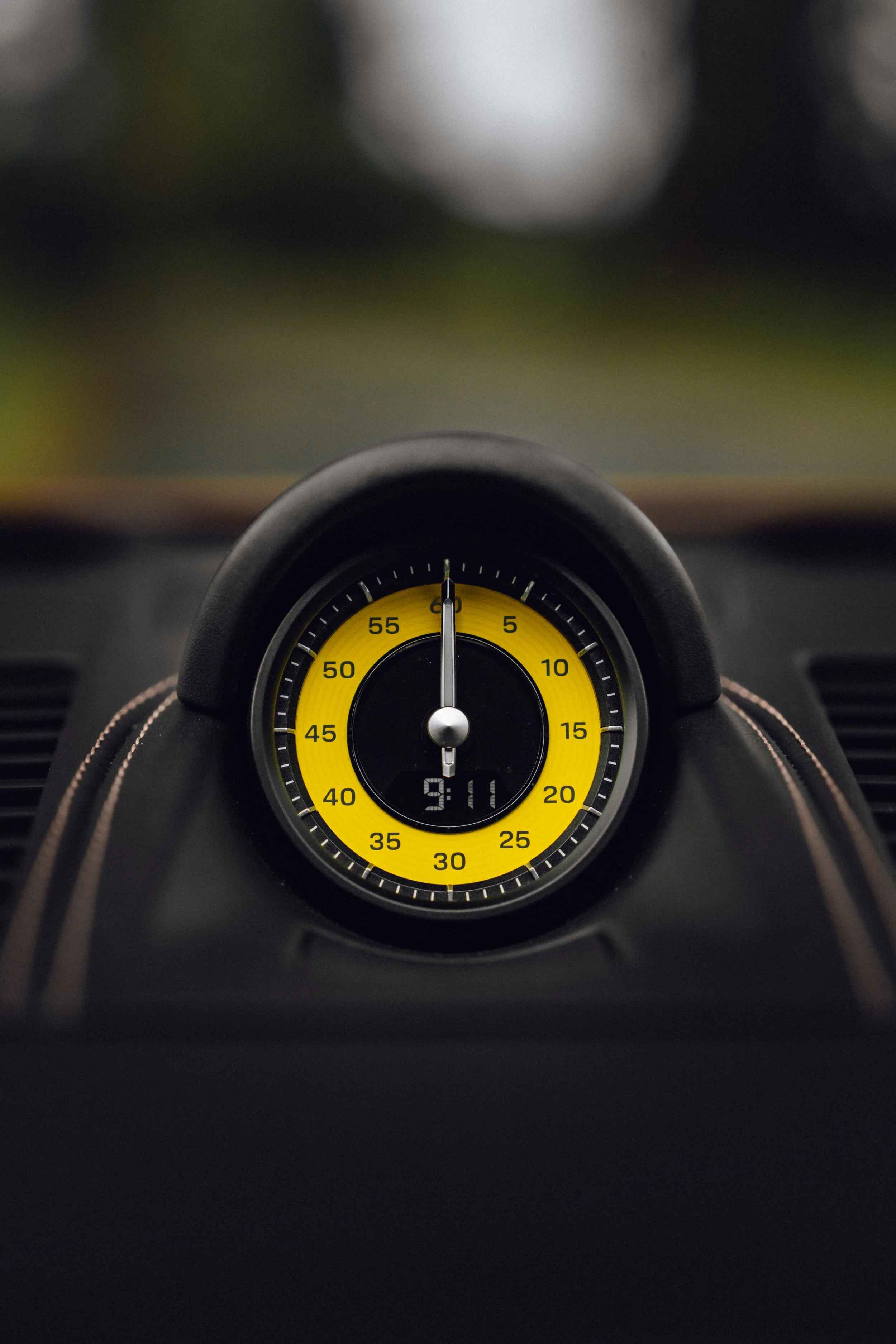 A car's analog clock with a yellow background, black numbers, and a digital display showing 9:11, mounted on a dashboard.