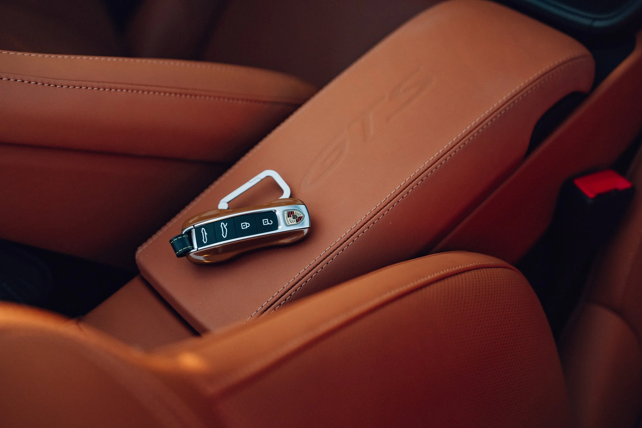 A Porsche car key resting on a tan leather car seat.