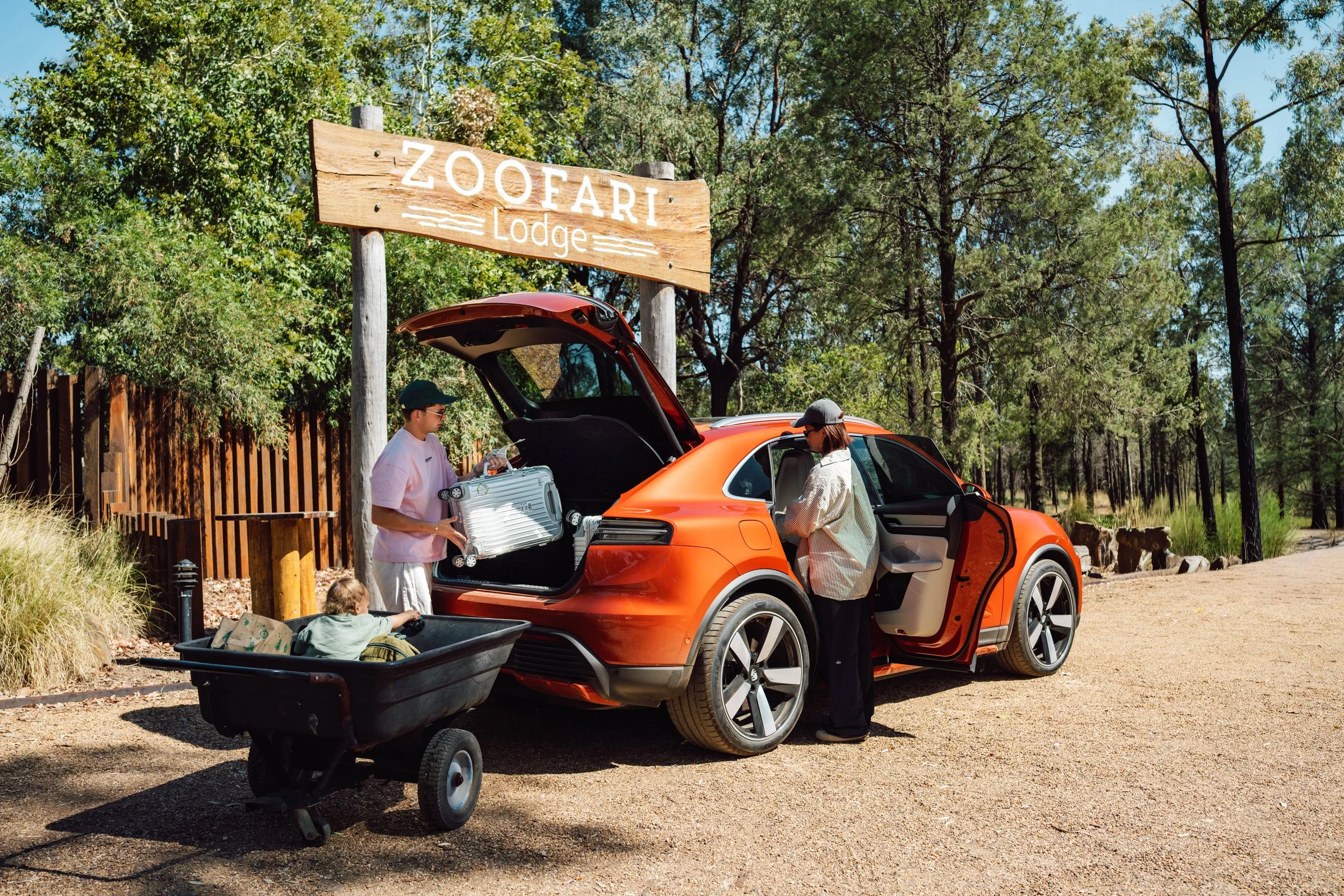 Family loading luggage into an orange electric vehicle at Zoofari Lodge entrance, surrounded by trees.