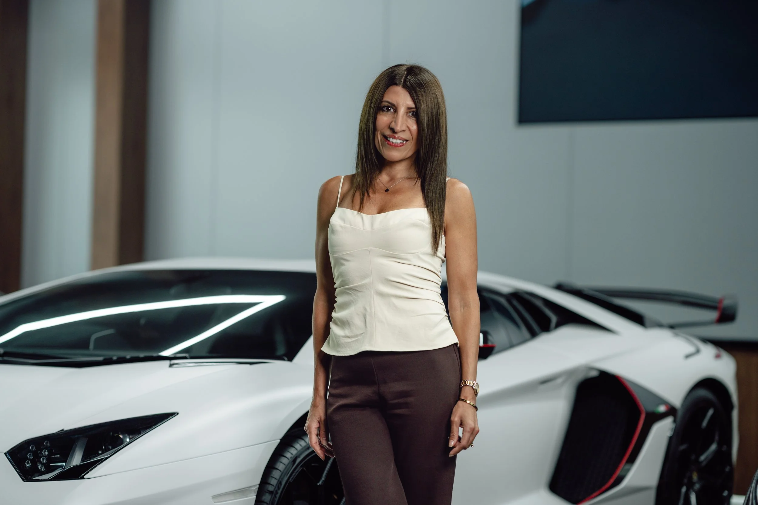 A woman standing in front of a white sports car in an indoor setting.