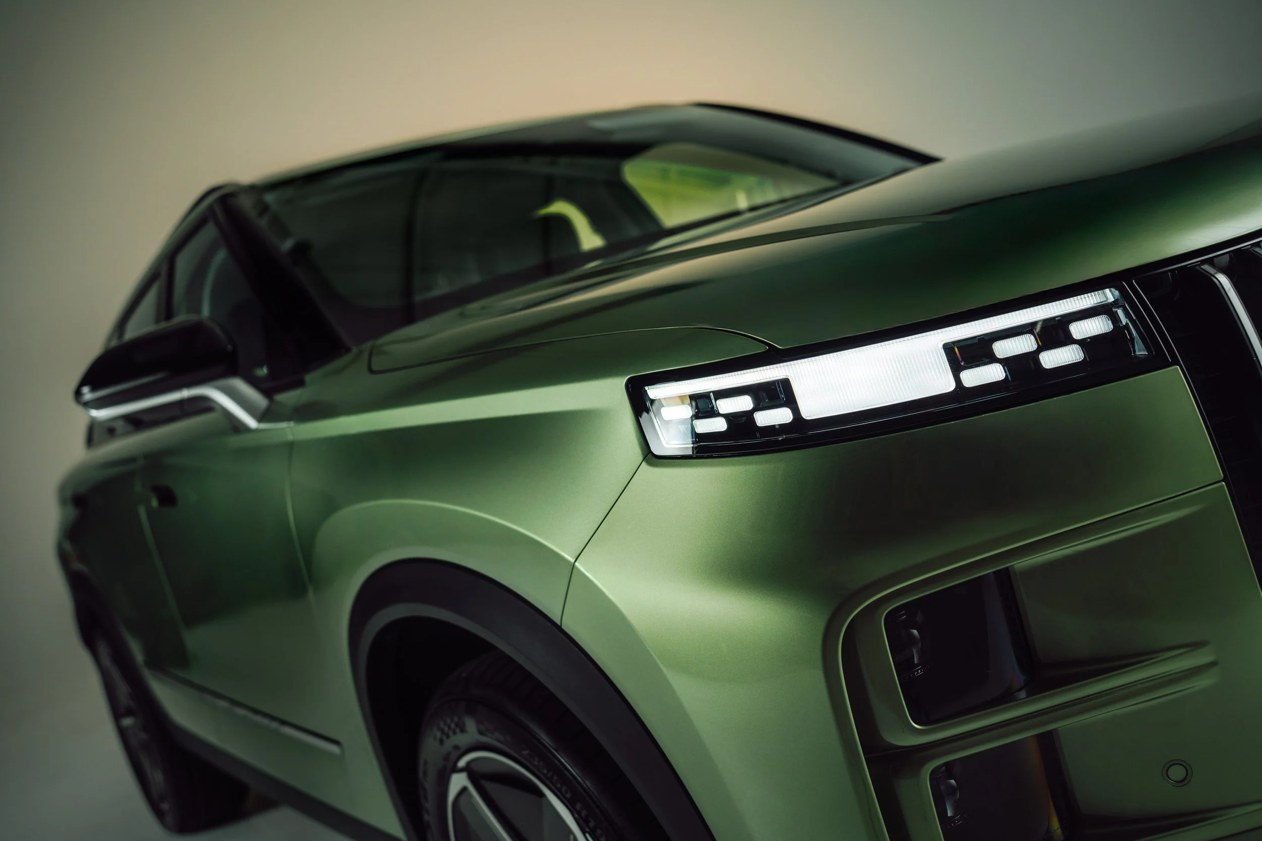 Close-up of front side of a green modern SUV with distinctive LED headlights and black accents.