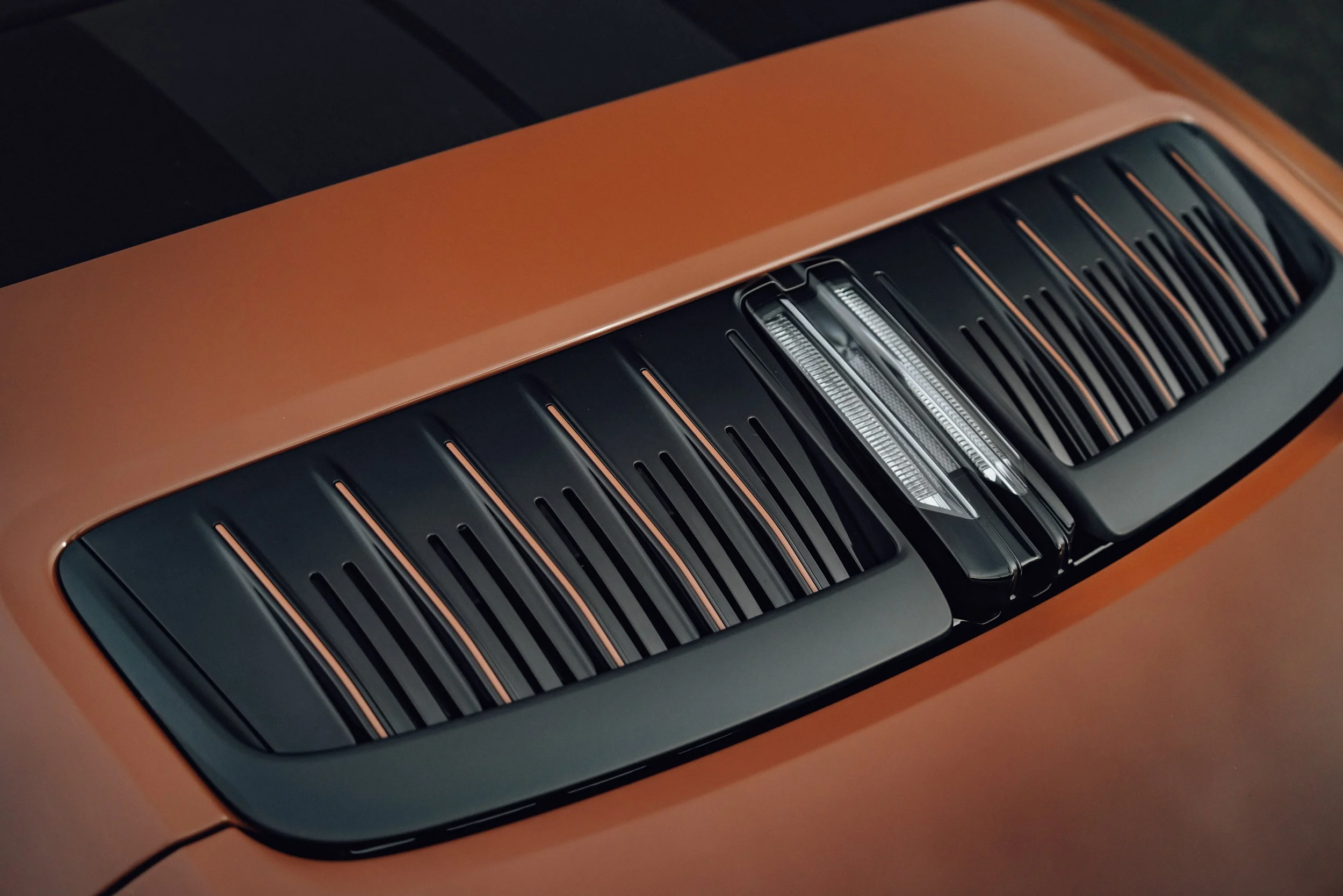 Close-up of an orange car with black and chrome vents on the hood