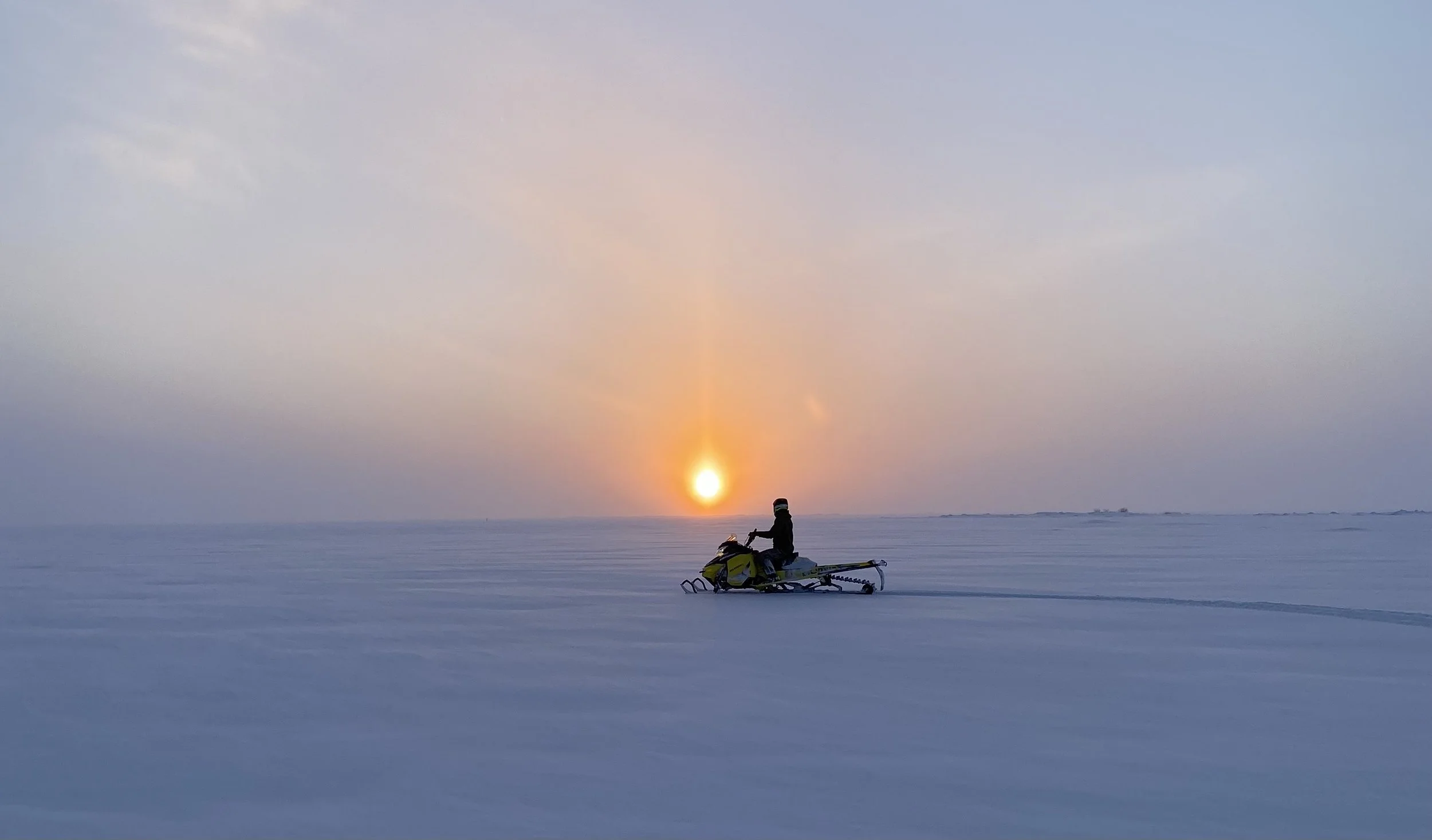 Sunsetting on frozen arctic sea and a snowmobiler.
