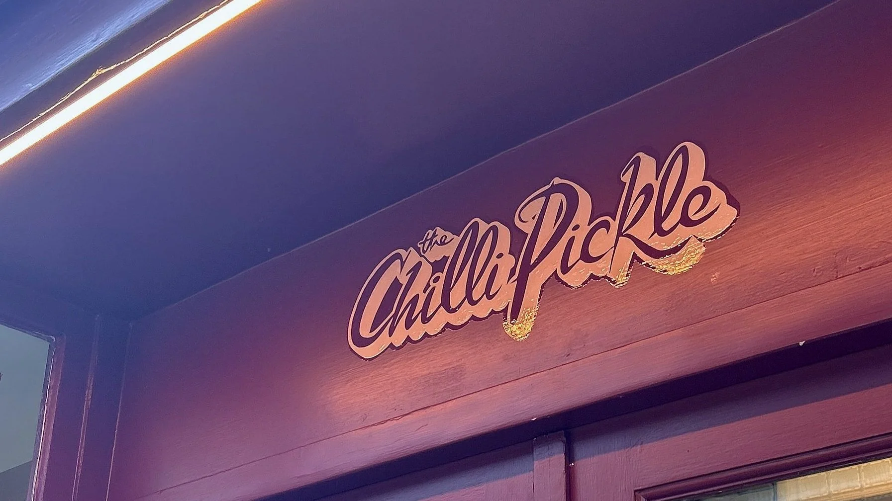 Close-up of a sign that says 'the Chili Pikkle' in stylized cursive font attached to the outside of a building.
