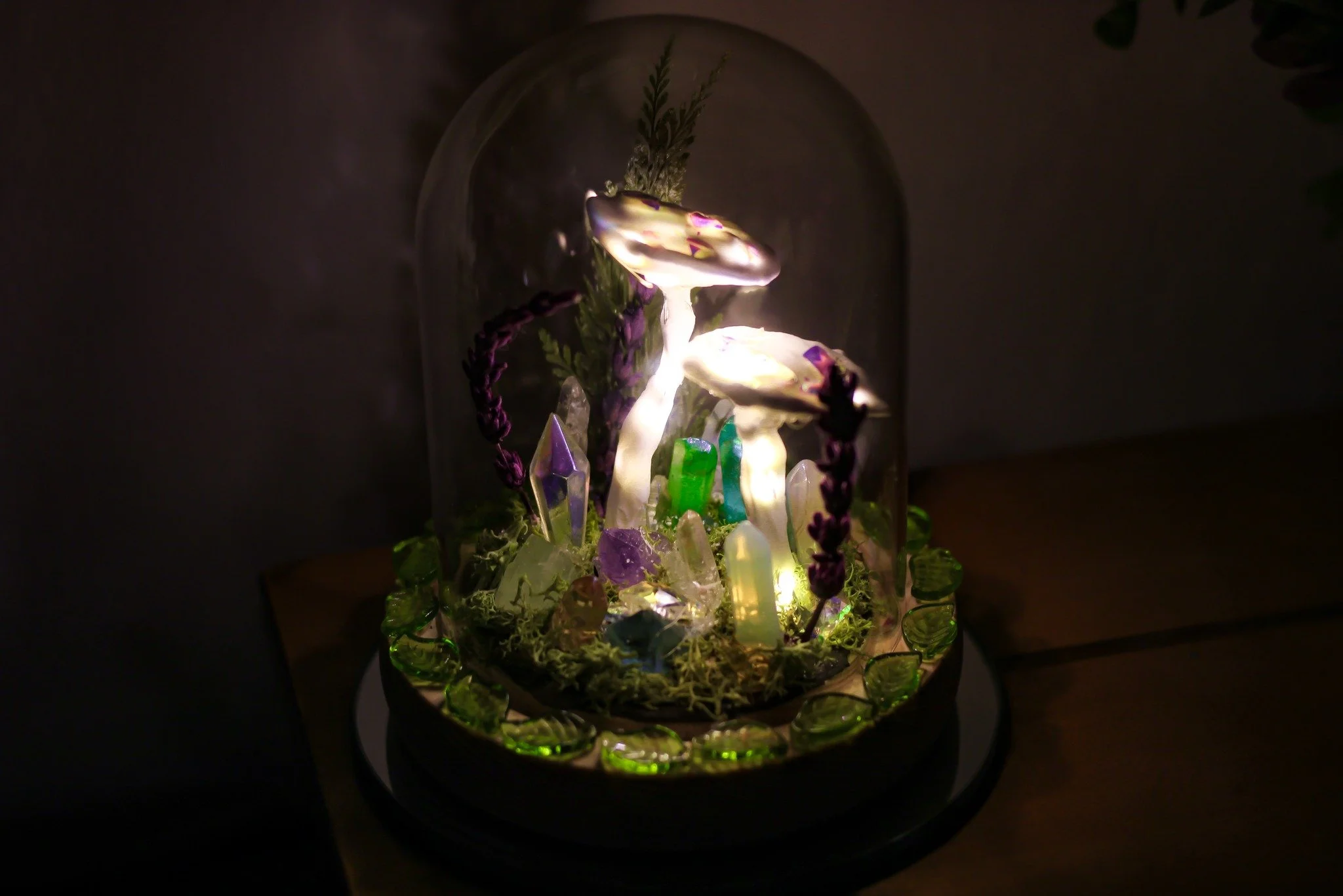 This is the second little terrarium light I've made. ✨🍄

It's full of treasures I love&mdash;pressed leaves, lavender, and sparkling gemstones. The little leaves surrounding the base are all genuine peridot as well! The mushrooms I made with modelin