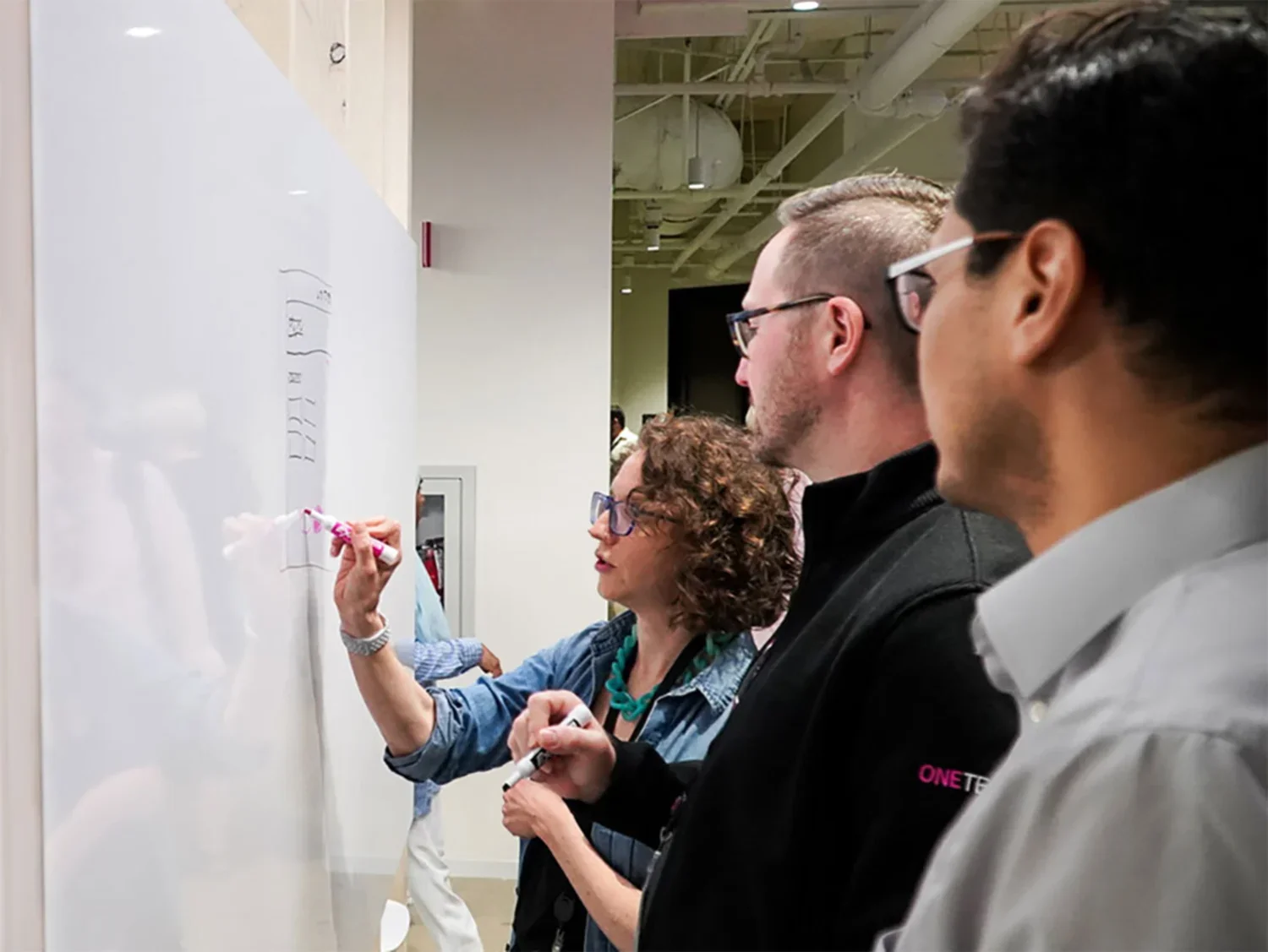 Two people looking at a third drawling on a whiteboard.